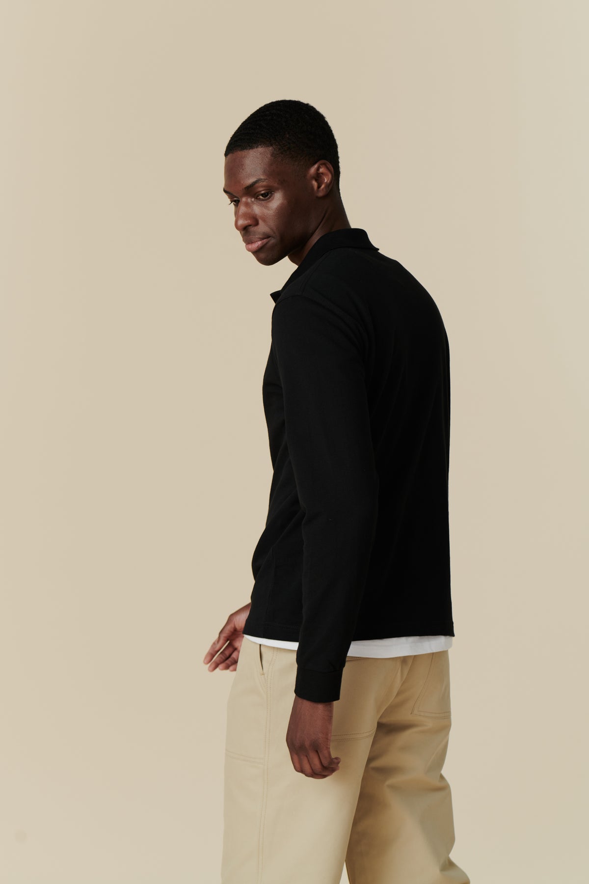 Side angle body image of man wearing black long sleeve polo shirt paired with a combat pant in putty
