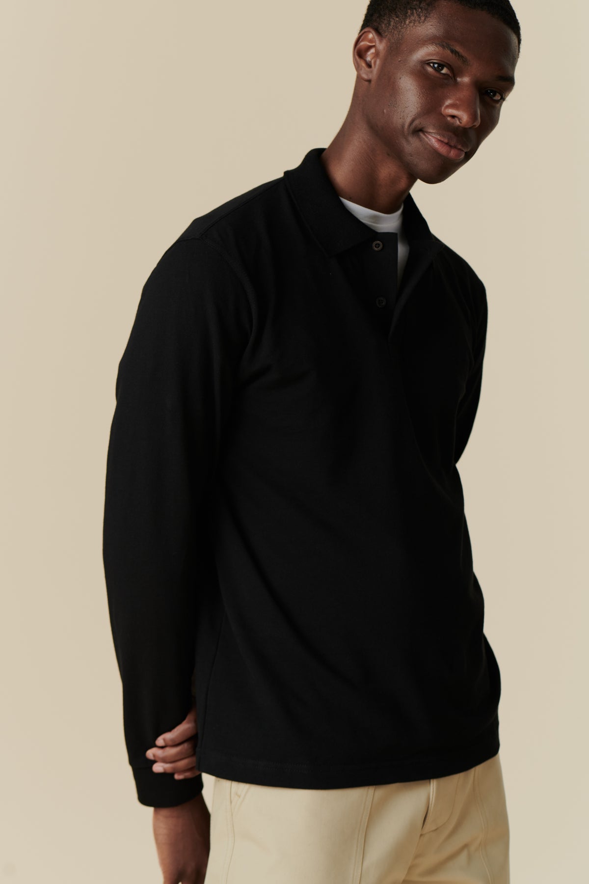 Thigh up image of black man wearing an unbuttoned black polo shirt with arms behind back