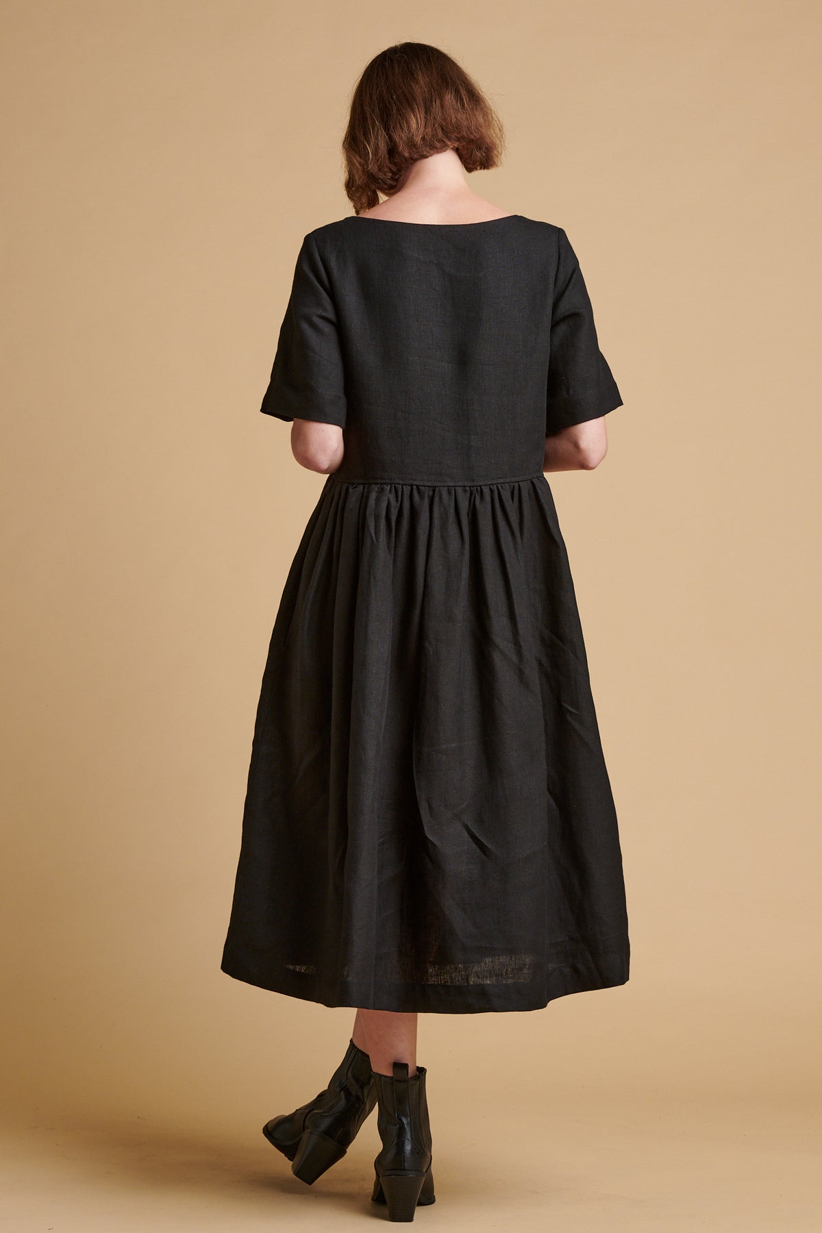 The back of female wearing crew neck gathered dress in black linen.