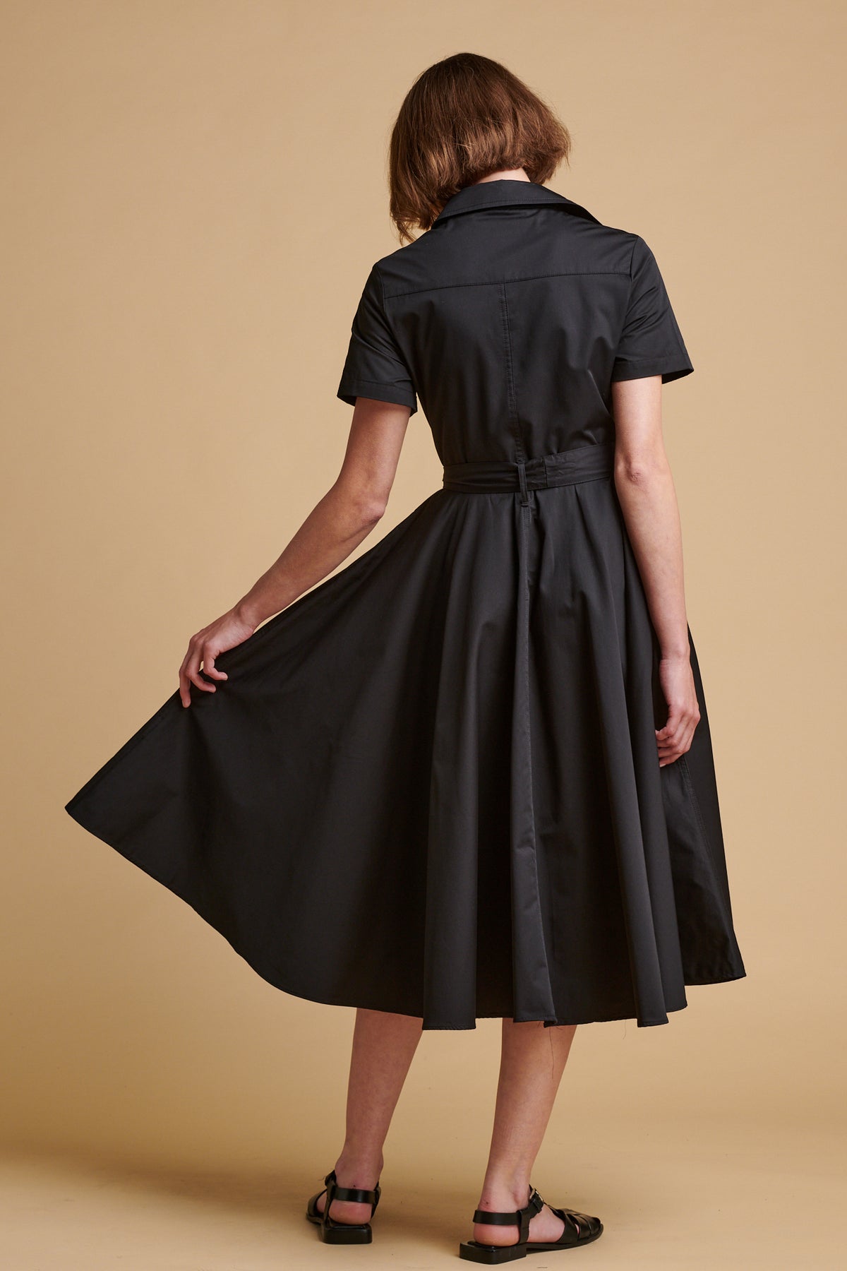 The back of female wearing full skirted phoebe trench dress in black.