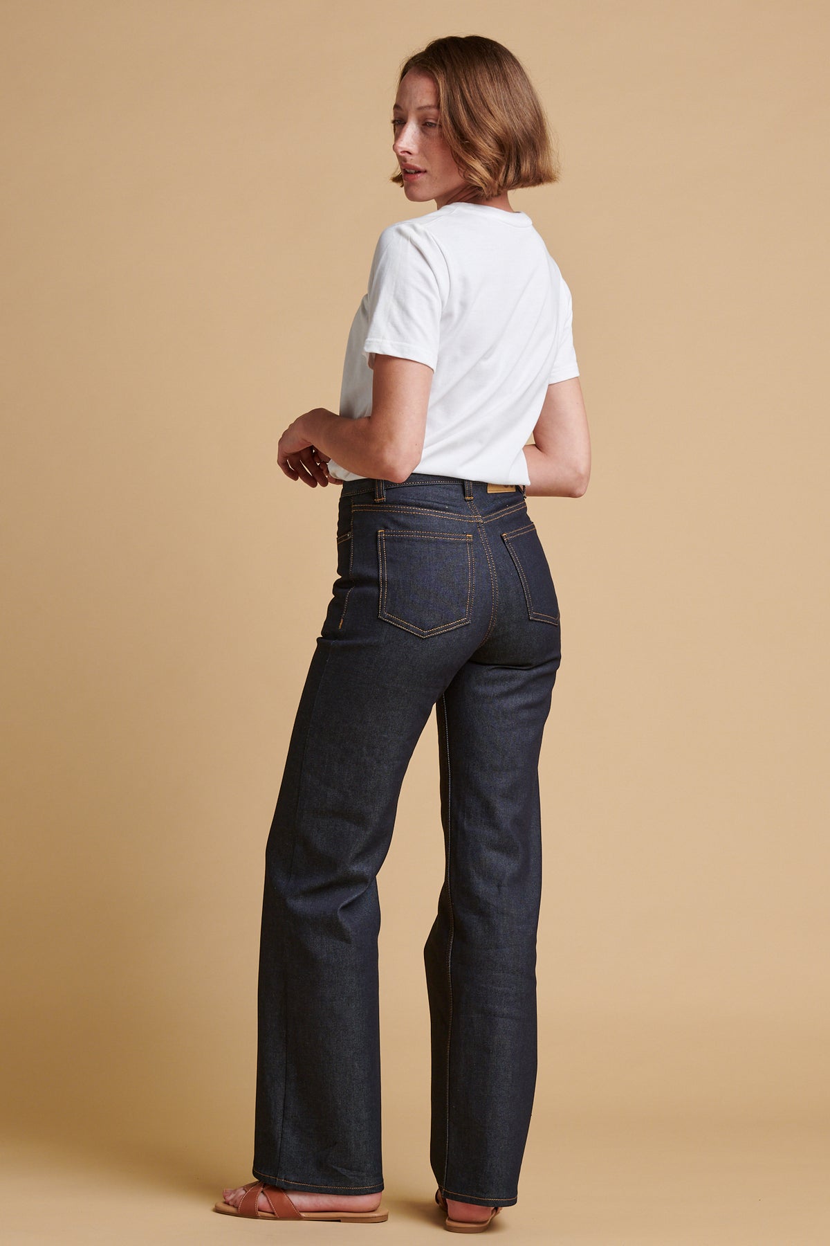 The back of female wearing wide leg high rise denim jean in indigo paired with classic short sleeve t shirt in white.