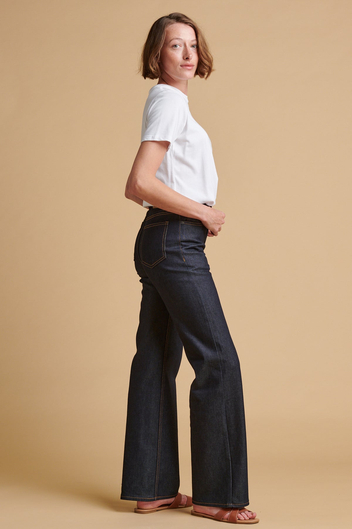 The side of female wearing wide leg high rise denim jean in indigo paired with classic short sleeve t shirt in white.