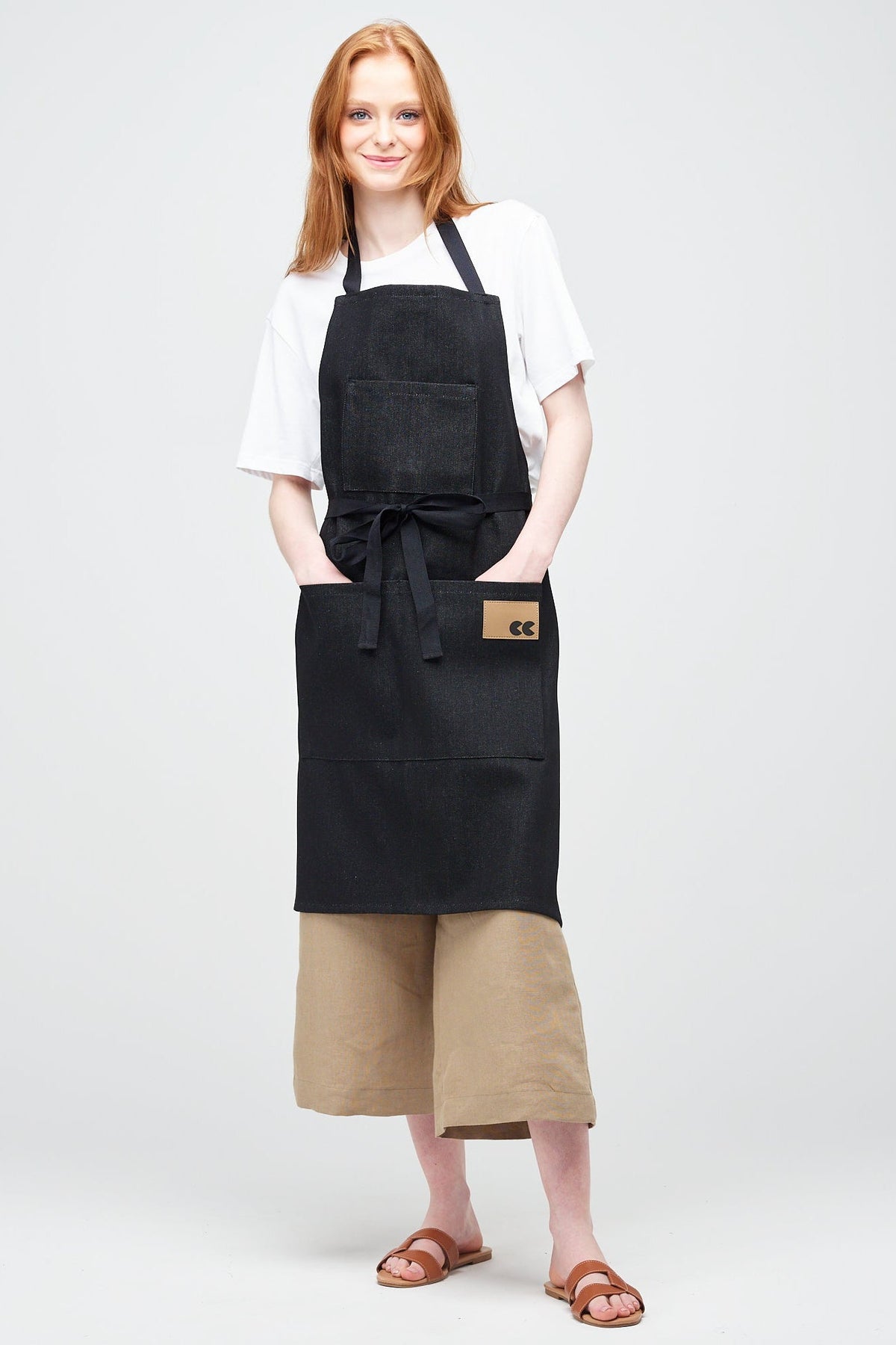 White Female with ginger hair wearing Apron in Black Denim with her hands in the front pocket