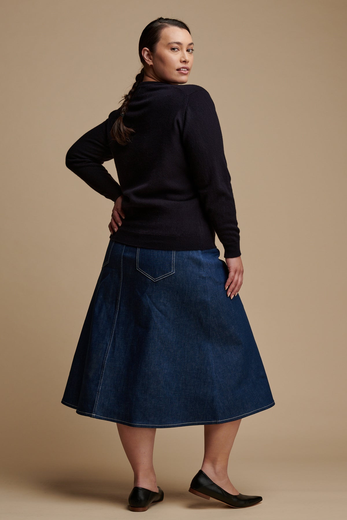 
            Female with back to the camera with brown hair tied back into a plait, looking back over her shoulder, wearing lambswool crew neck in navy paired with Bobbie A line mini skirt in blue.