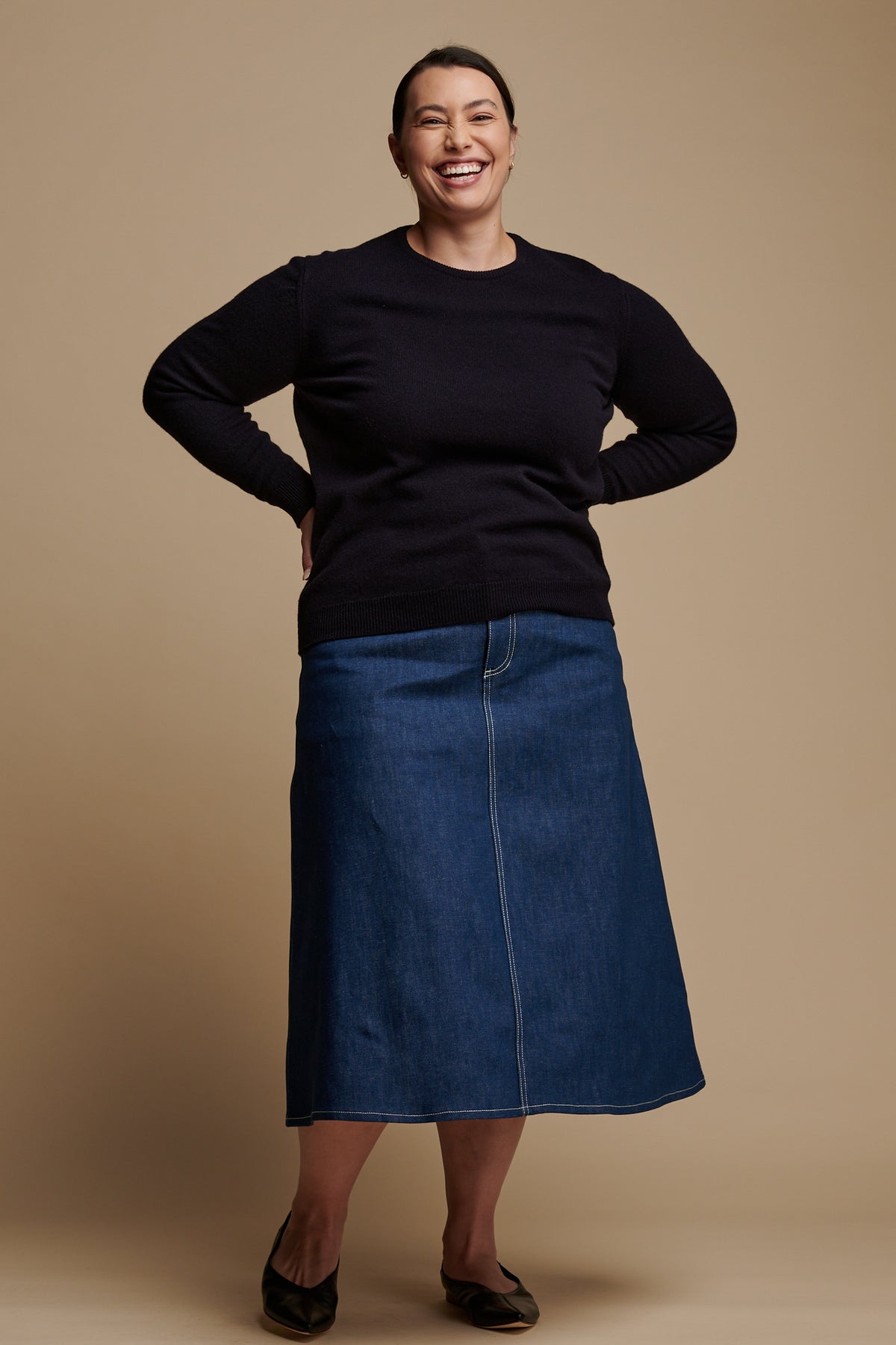 Smiley female with her hands on hips wearing Bobbie A line denim skirt in blue paired with lambswool crew neck in navy.
