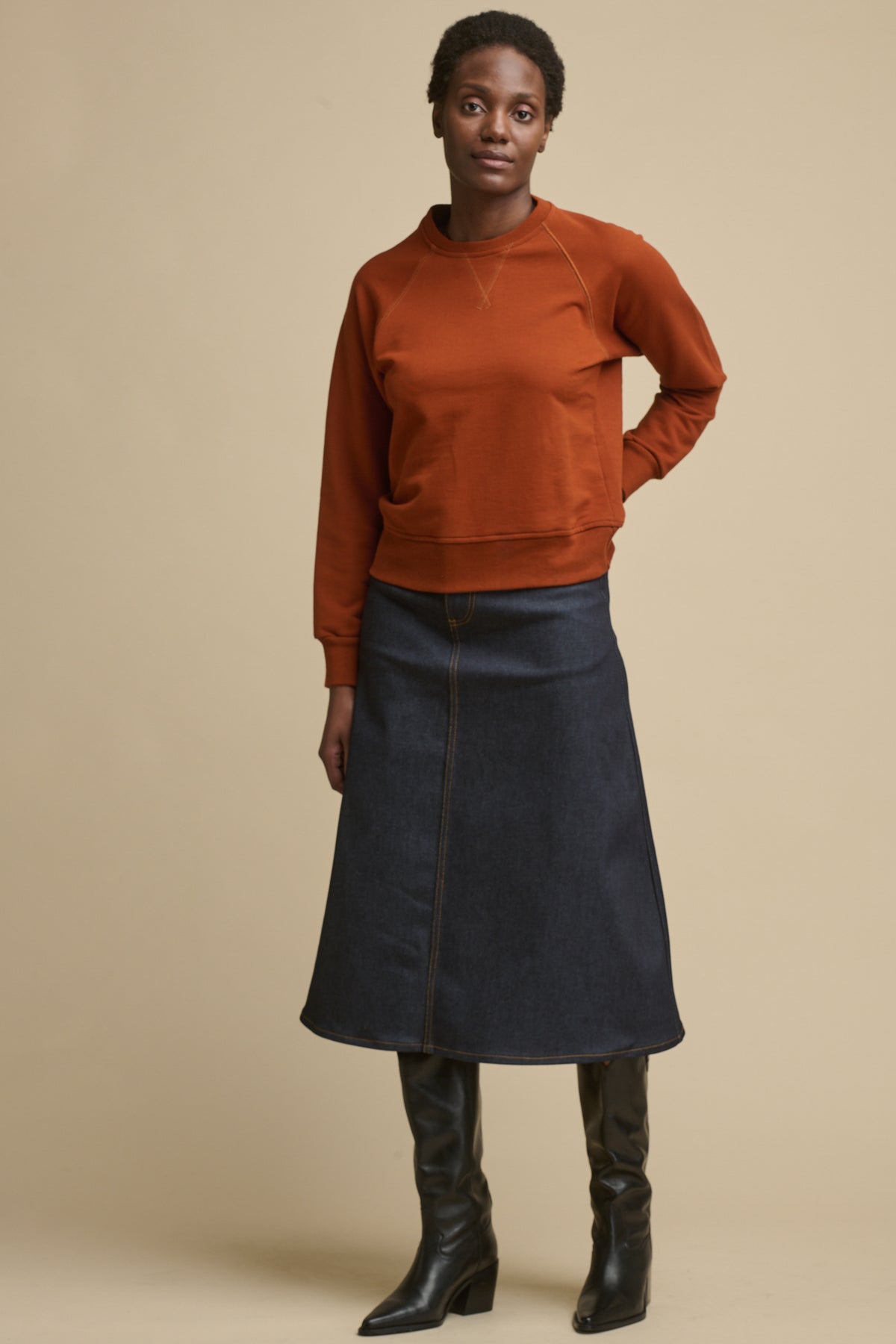 Full body image of the front of black female wearing Bobbie a line denim skirt in indigo paired with cinnamon raglan sweatshirt