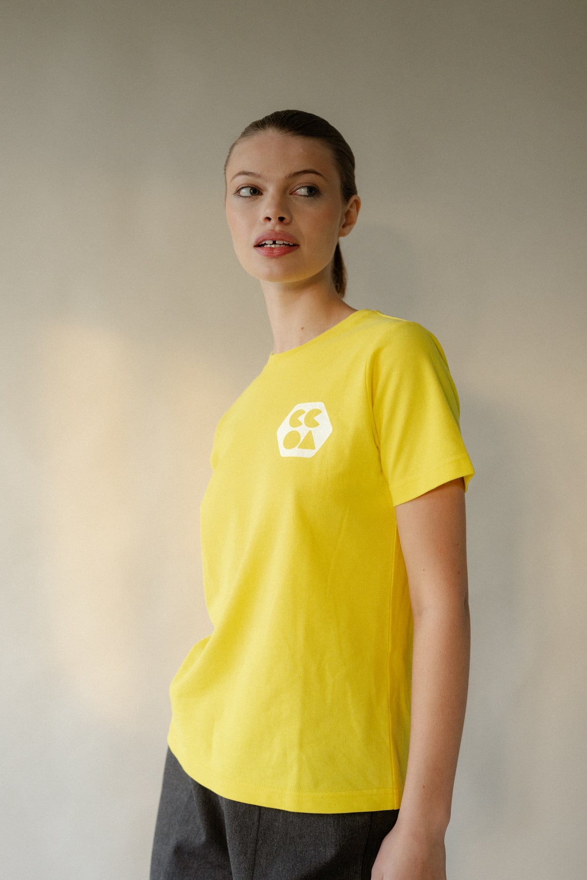 
            Thigh up image of female wearing women&#39;s breathable short sleeve t shirt plastic free in canary yellow with white CCOA logo