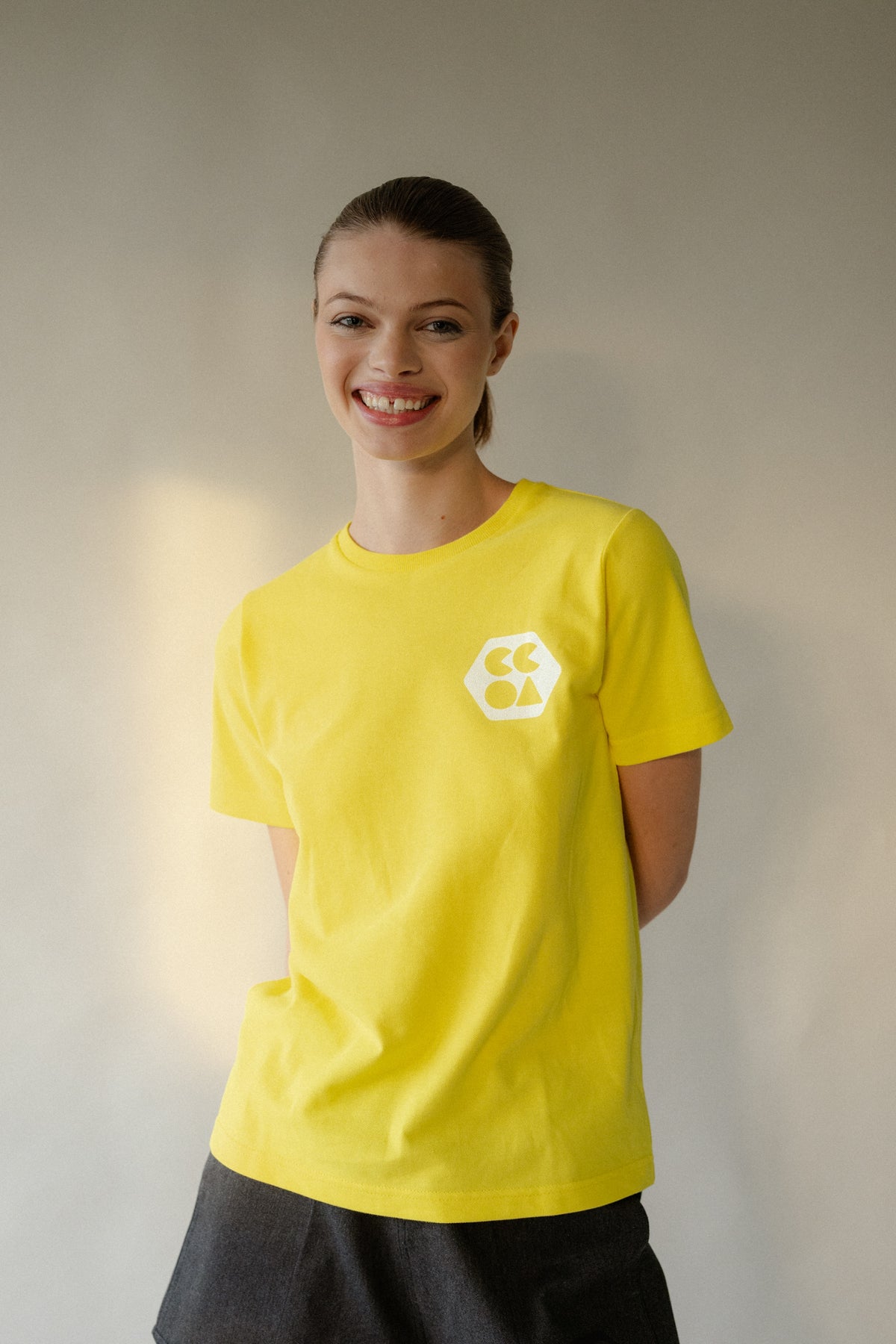 Thigh up image of smiley female wearing women's breathable short sleeve t shirt plastic free in canary yellow with white CCOA logo