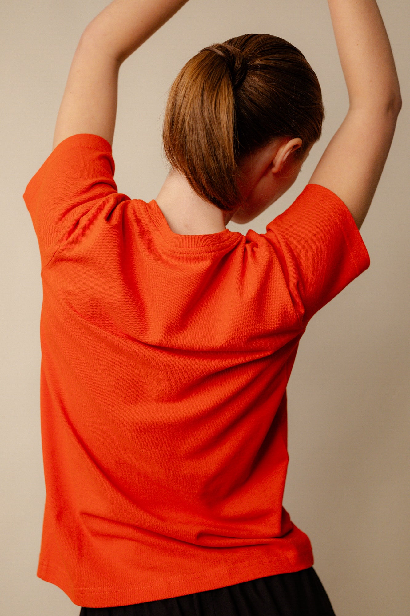 Back of female stretching arms up wearing breathable t shirt in flame red