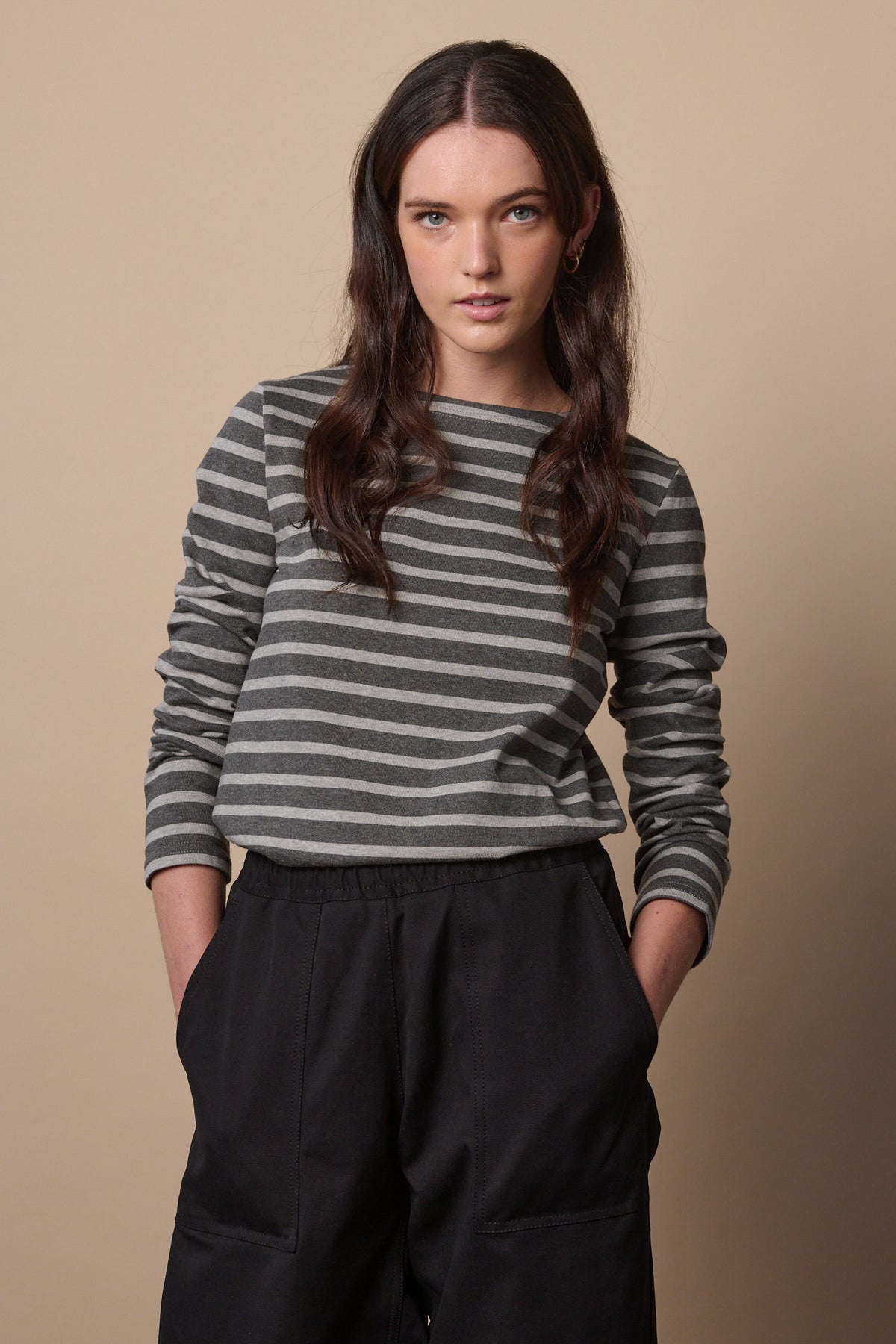 White female with long brunette hair wearing Breton in charcoal marl and grey marl tucked into trousers with sleeves pushed up the arm