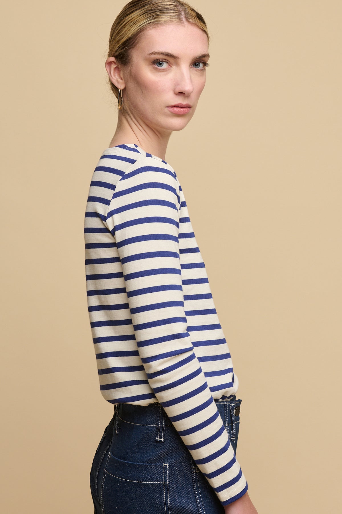 Thigh up image of female from the side wearing Breton in ecru/bright blue tucked into women's work jeans in blue