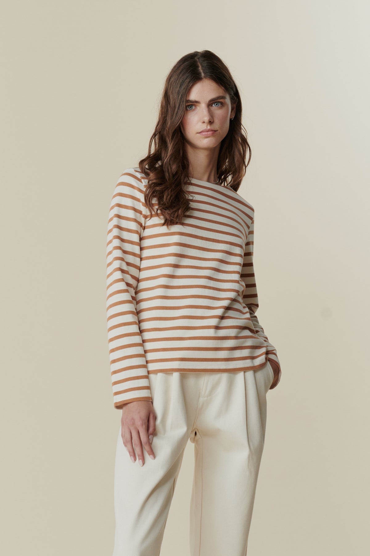 Brunette female wearing Breton in ecru cinnamon stripe paired with pleated jeans in ecru