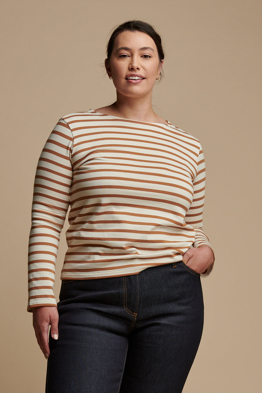 
            Thigh up of female with brown hair tied back into a low ponytail wearing long sleeve Breton top in ecru and cinnamon stripes paired with work jean in indigo.