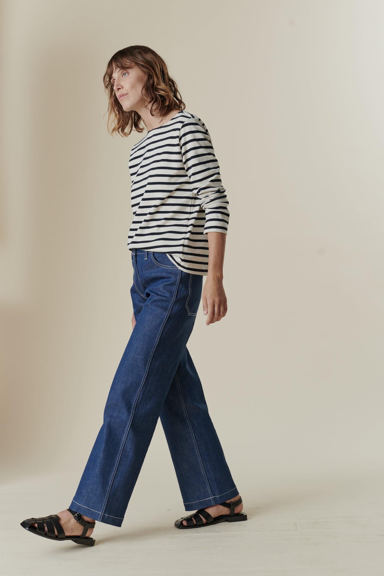 Full body image of female wearing breton in ecru navy stripe paired with women's work jean in blue
