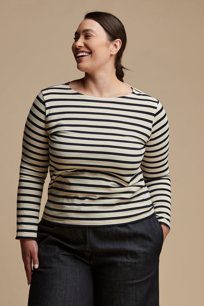 
            Thigh up of smiley female wearing long sleeve Breton top with boat neck in ecru navy stripes paired with indigo denim trousers