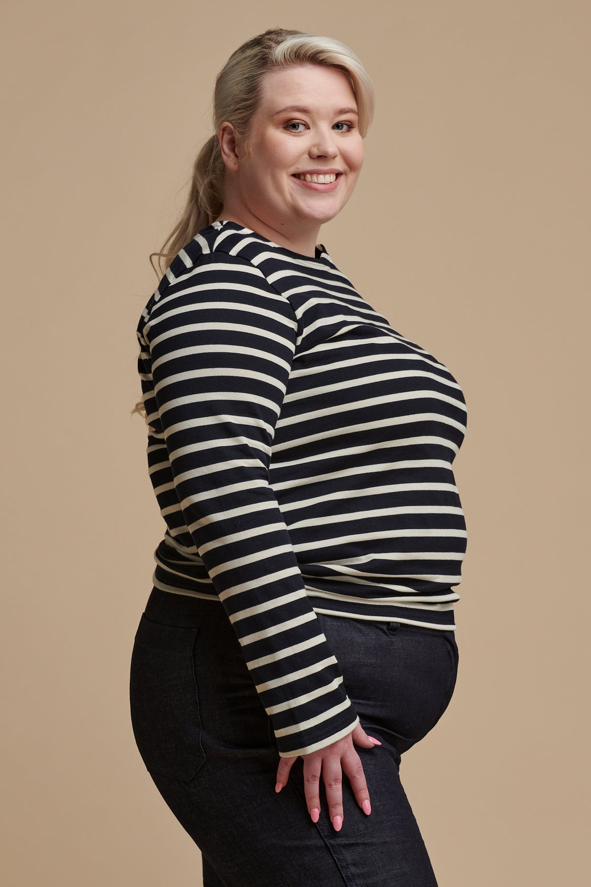 Thigh up of the side of female wearing long sleeve Breton top in navy ecru stripe paired with work trousers in indigo denim
