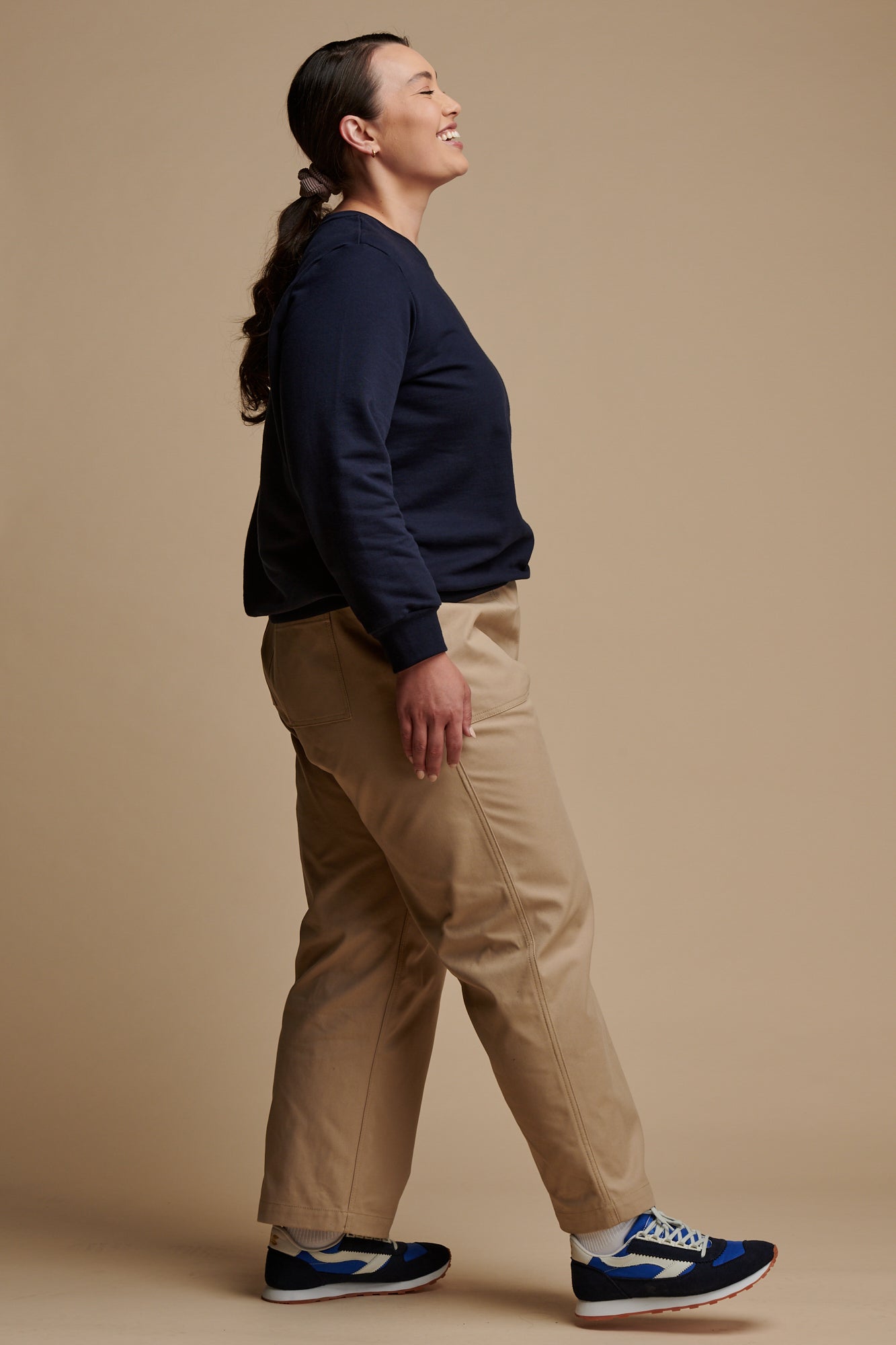Full body image of the front of smiley female wearing camerawoman drawstring tapered cotton canvas trousers in putty paired with navy sweatshirt.