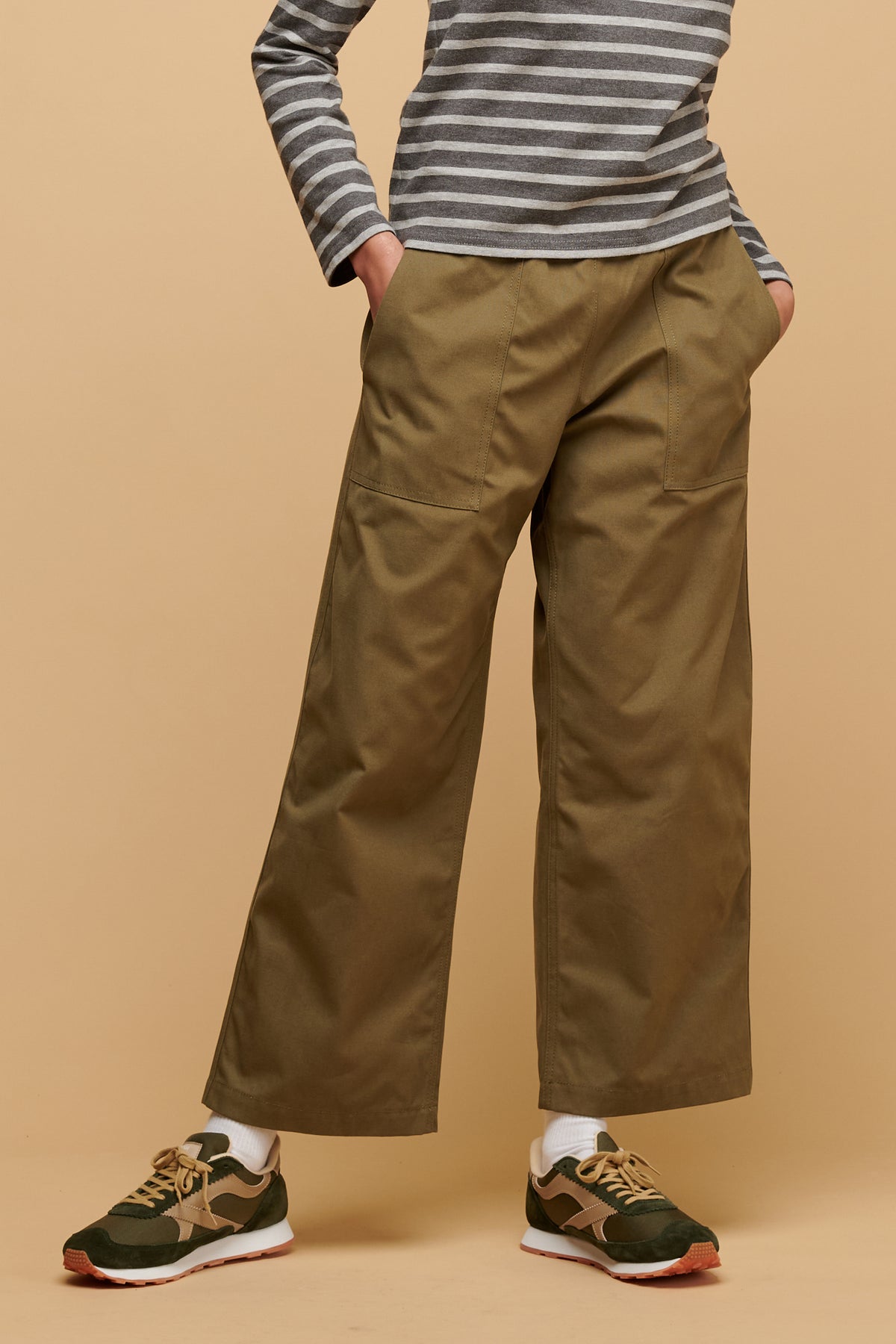 Chest down of female wearing community clothing camerawoman drawstring tapered cotton canvas trousers in olive paired with beacon trainers in olive/beige