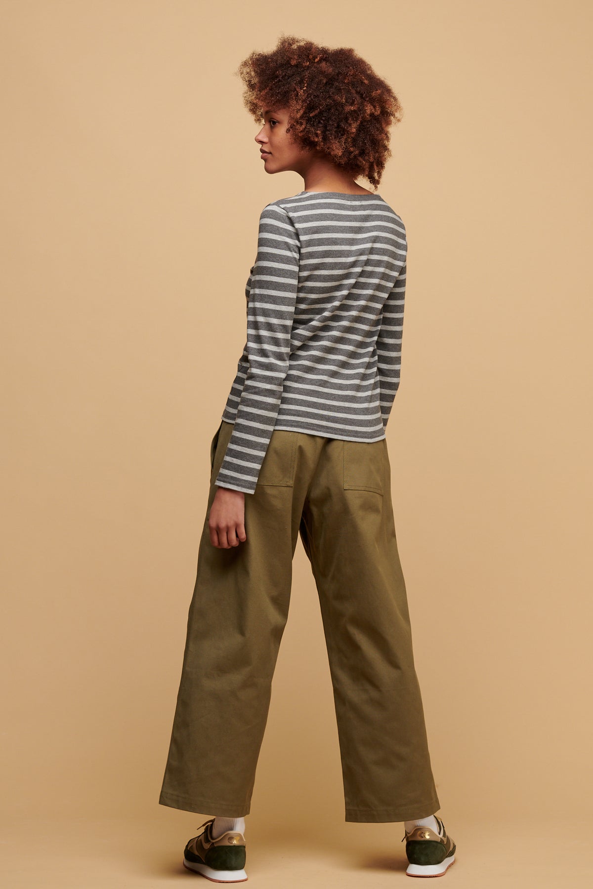 the back of female wearing community clothing camerawoman drawstring tapered cotton canvas trousers in olive paired with women's Breton in charcoal grey with Beacon trainers in olive/beige.