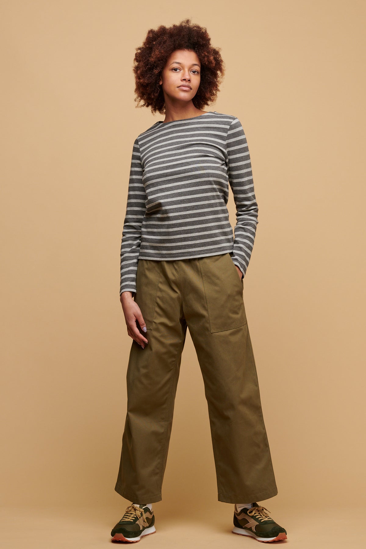 Female wearing community clothing camerawoman drawstring tapered cotton canvas trousers in olive paired with women's Breton in charcoal grey with Beacon trainers in olive/beige