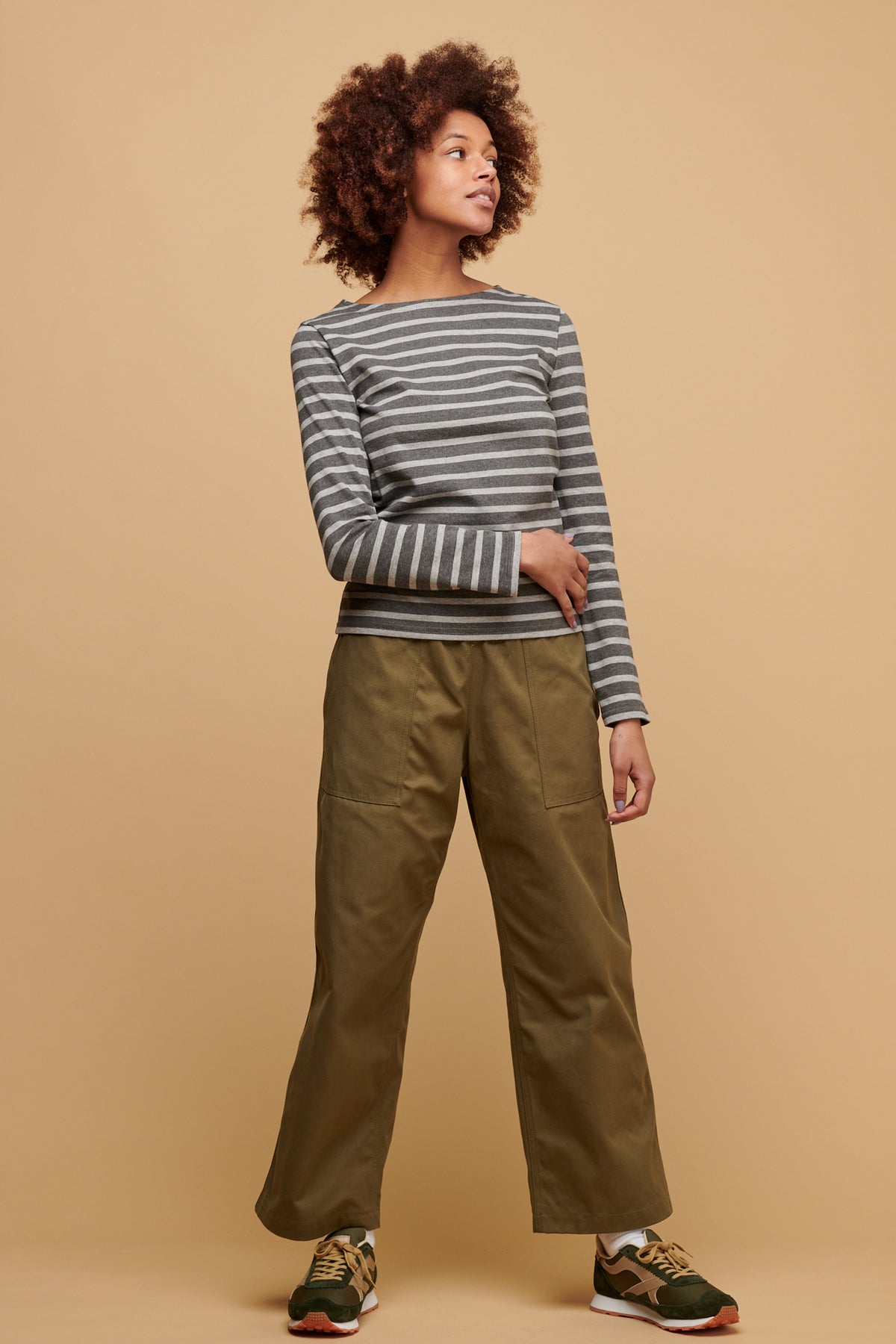 Female wearing community clothing camerawoman drawstring tapered cotton canvas trousers in olive paired with women's Breton in charcoal grey with Beacon trainers in olive/beige
