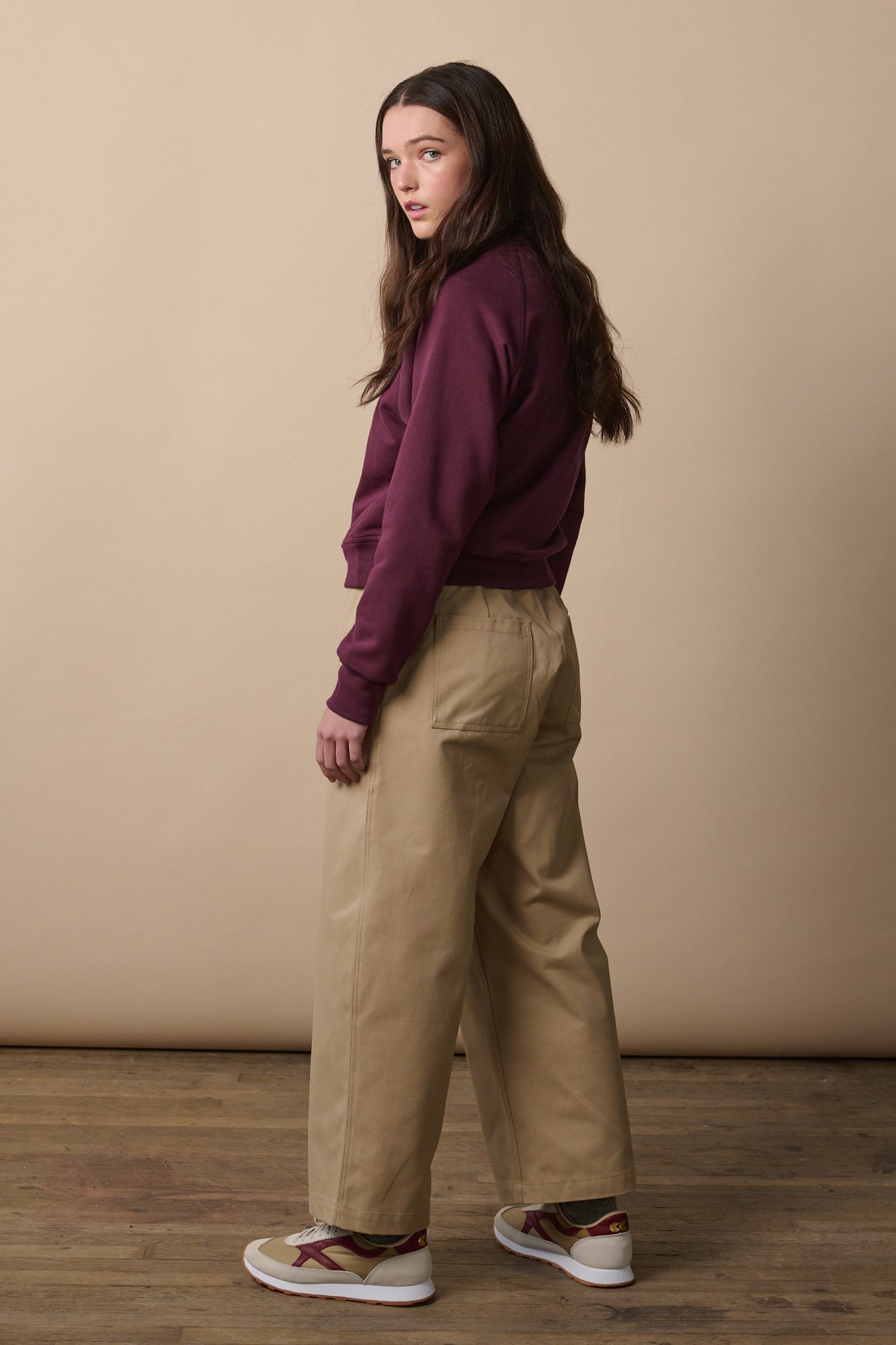 Image of female turned away from the camera showing the back of the wide tapered camerawoman drawstring trousers in putty. Two back pockets