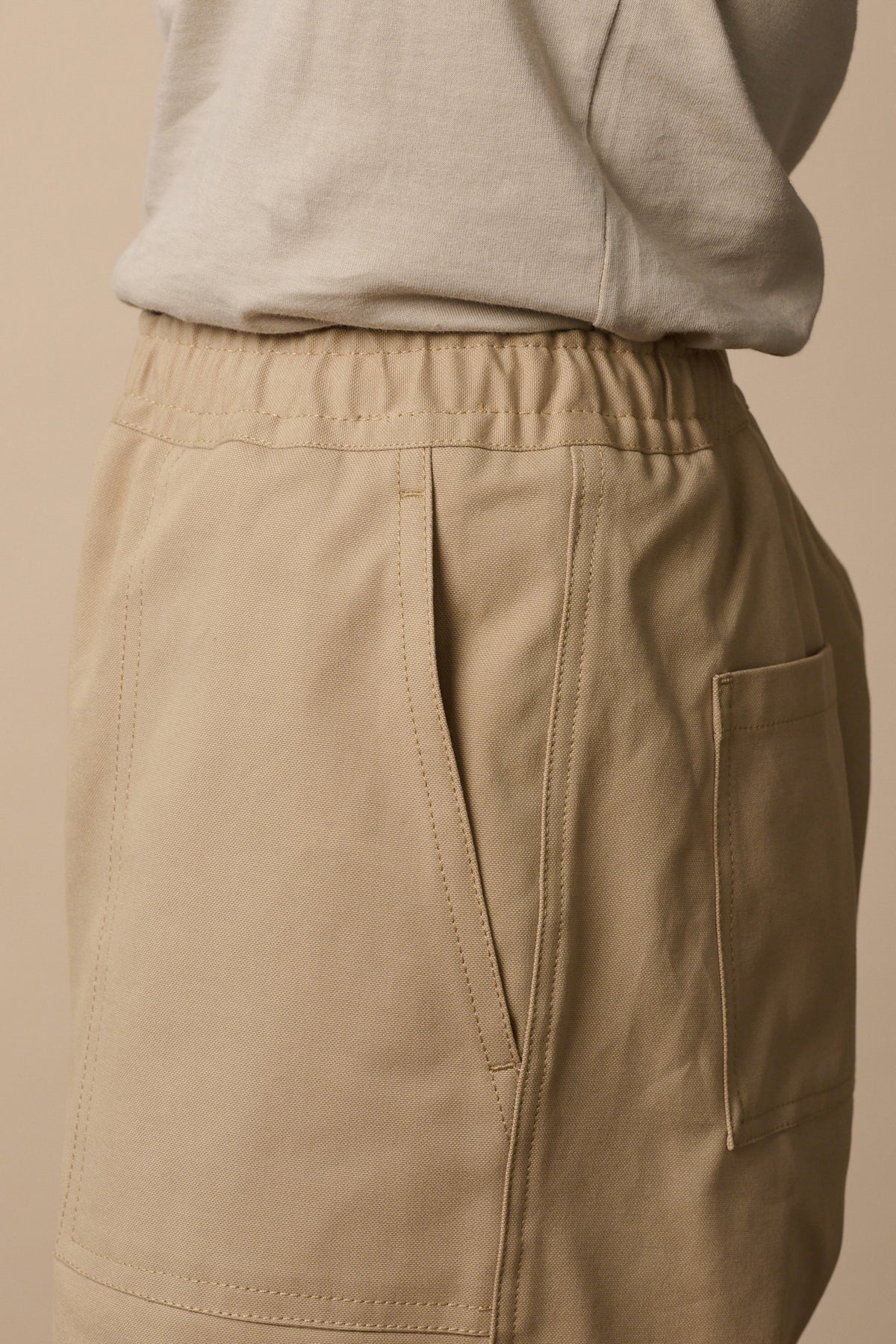 Close up of the side of the Camerwoman trousers in putty, drawstring waistband and front and back pockets.