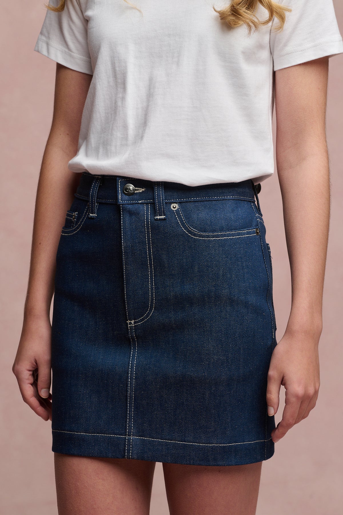 Close up of the front of female wearing Charlie denim mini skirt in blue, with white short sleeve t shirt tucked in.