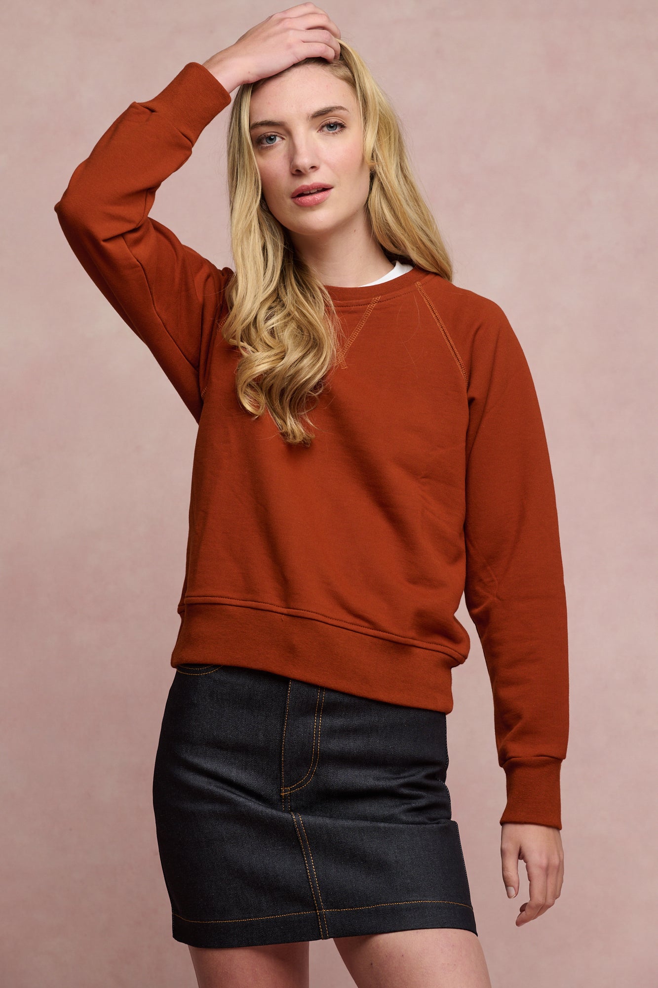 Thigh up image of the front of female wearing Charlie denim mini skirt in indigo paired with raglan sweatshirt in cinnamon