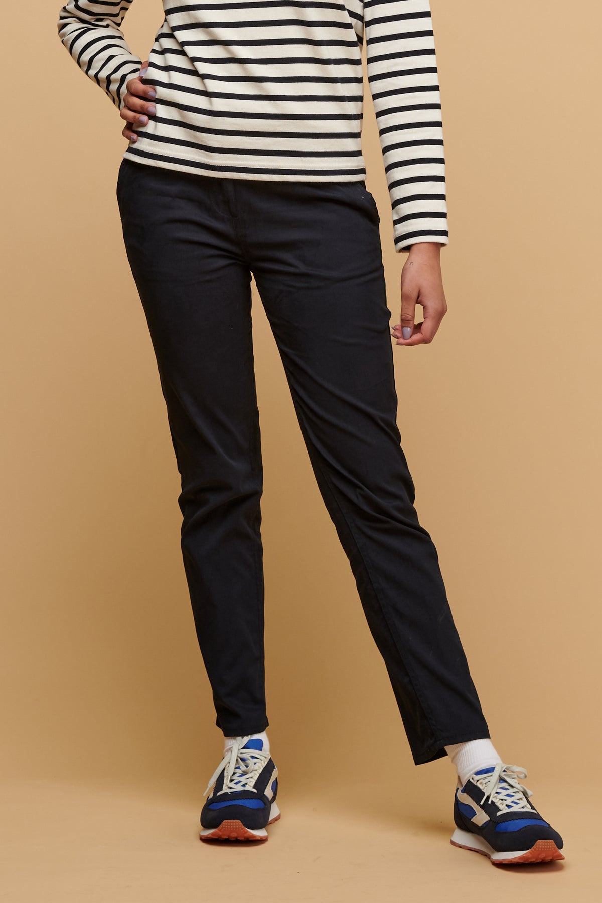 Chest down of the front of female wearing slim stretch chino in navy paired with Walsh X Community Clothing Parlick trainers.