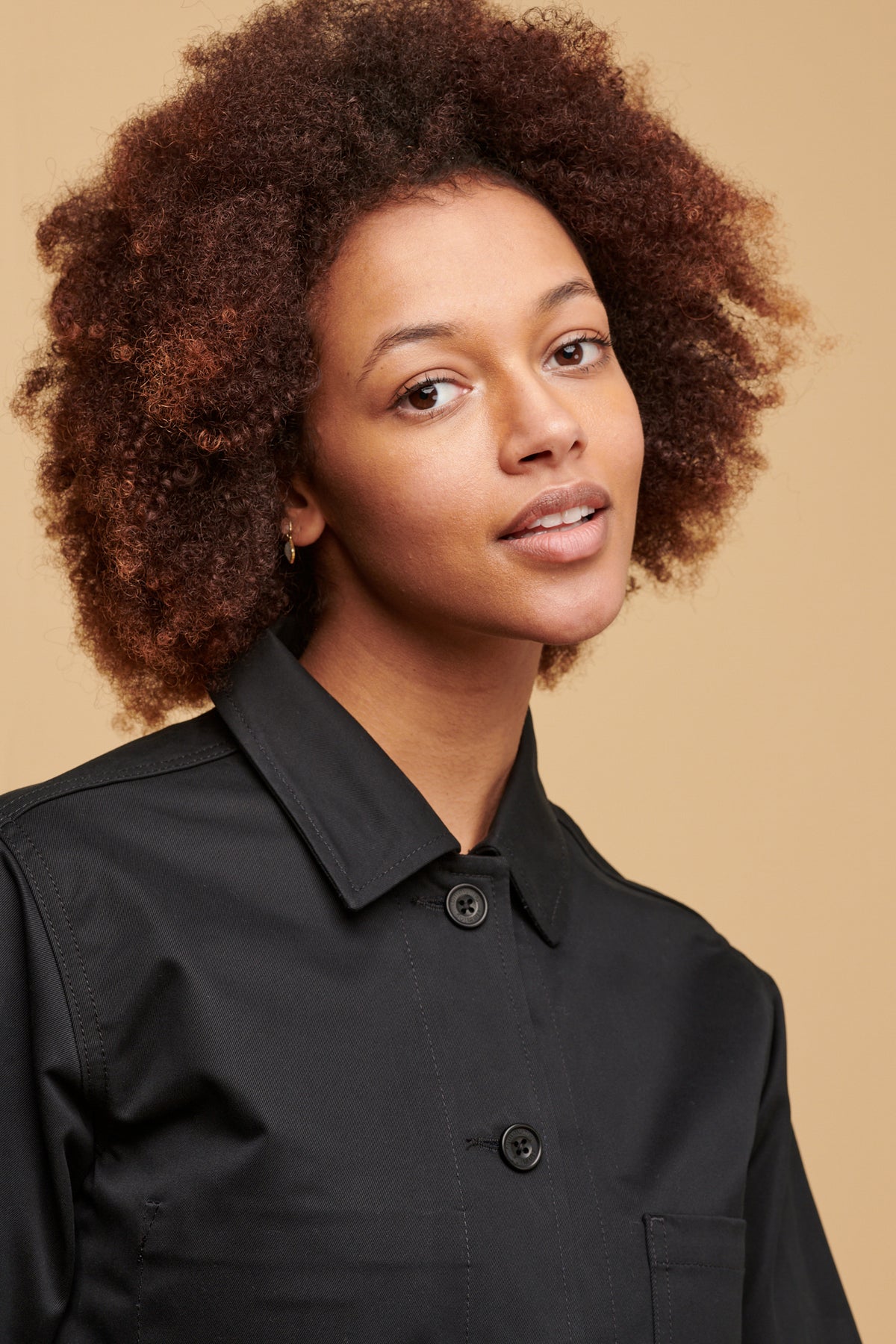 
            Portrait of female of colour with afro wearing buttoned up, chore jacket in black