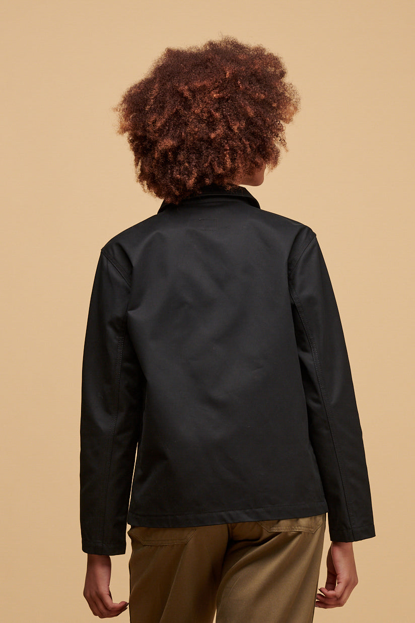 Thigh up of the back of female wearing chore jacket in black paired with work trousers in light olive