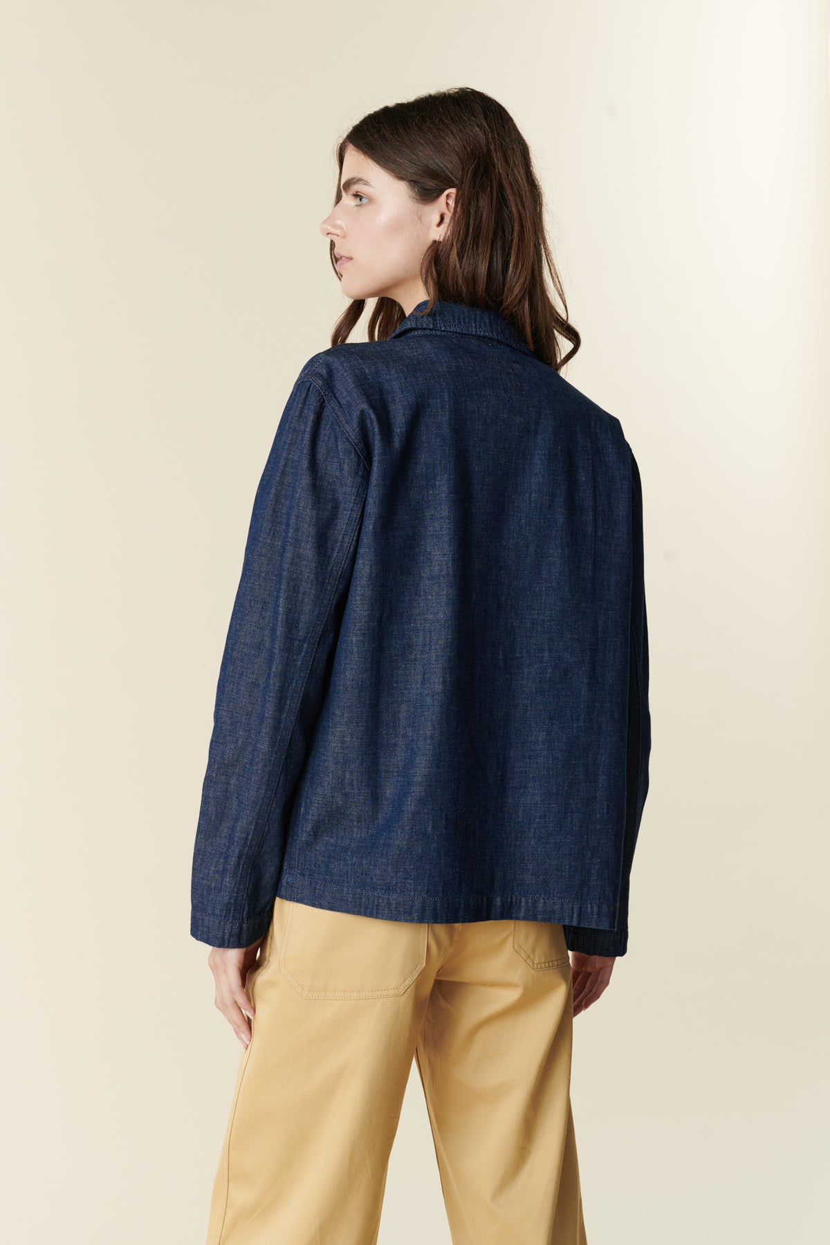 Back, thigh up image of brunette female wearing chore jacket in denim