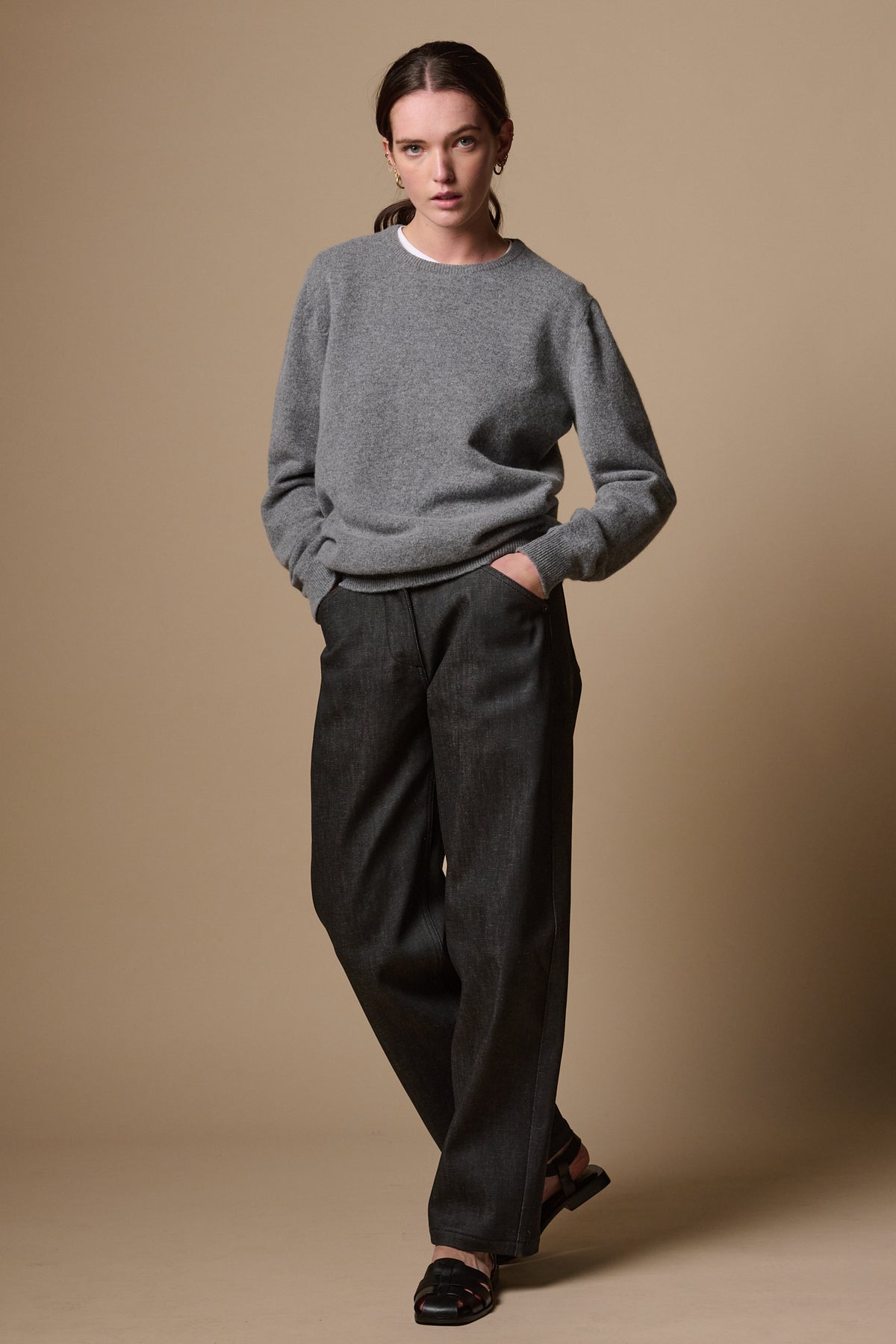 White female wearing chore wide tapered leg jeans in black, with hands in the two front pockets. Worn with lambswool crew neck jumper in grey