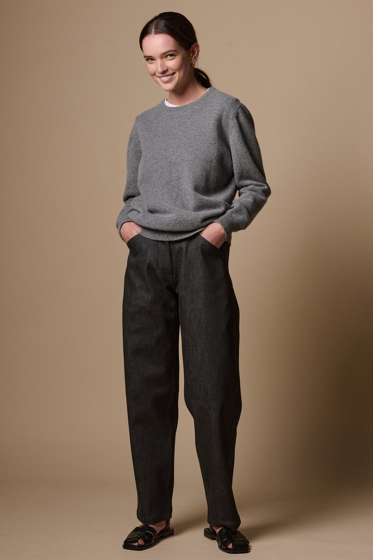White female wearing chore wide tapered leg jeans in black, with hands in the two front pockets. Worn with lambswool crew neck jumper in grey