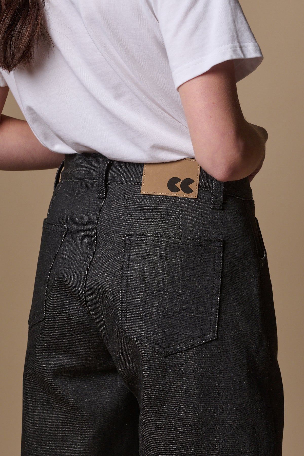 Detail shot of the back of women's chore jeans in black, showing brown jean patch with CC logo and belt loops, also two back pockets
