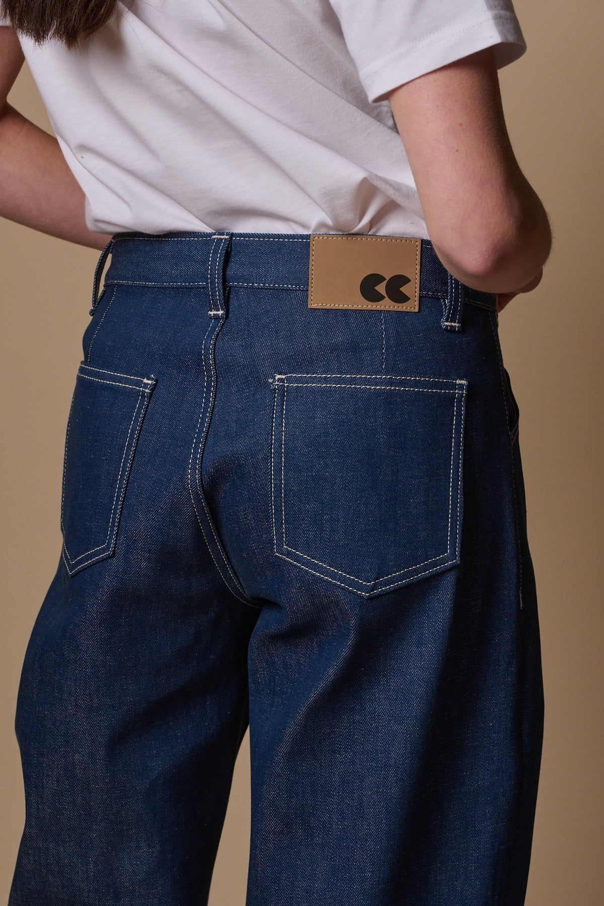 
            Close up of the back of chore jeans in blue showing two back pockets and jeans patch on waistband with belt loops. Contrast white stitching.