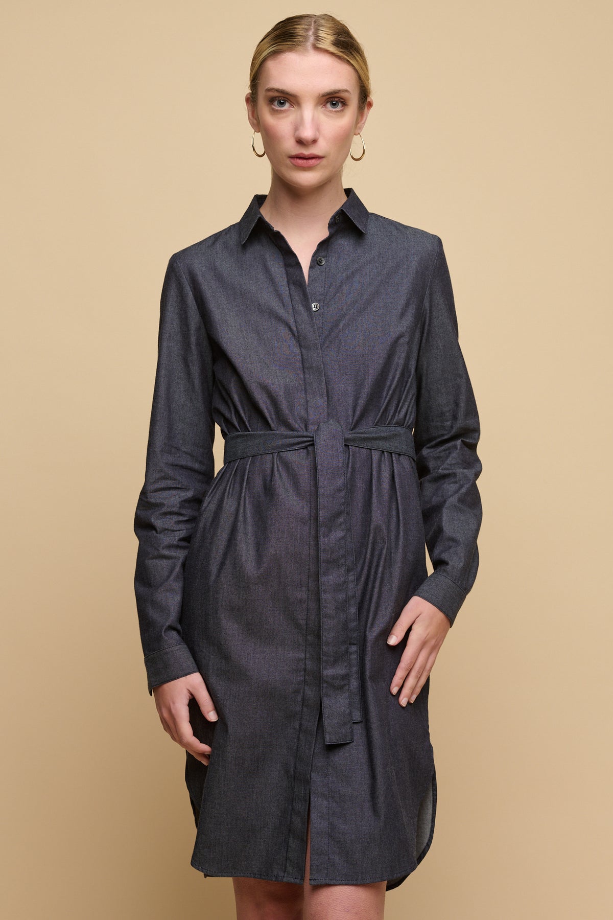 Knee up image of female wearing collared shirt dress in indigo with waist belt tied.
