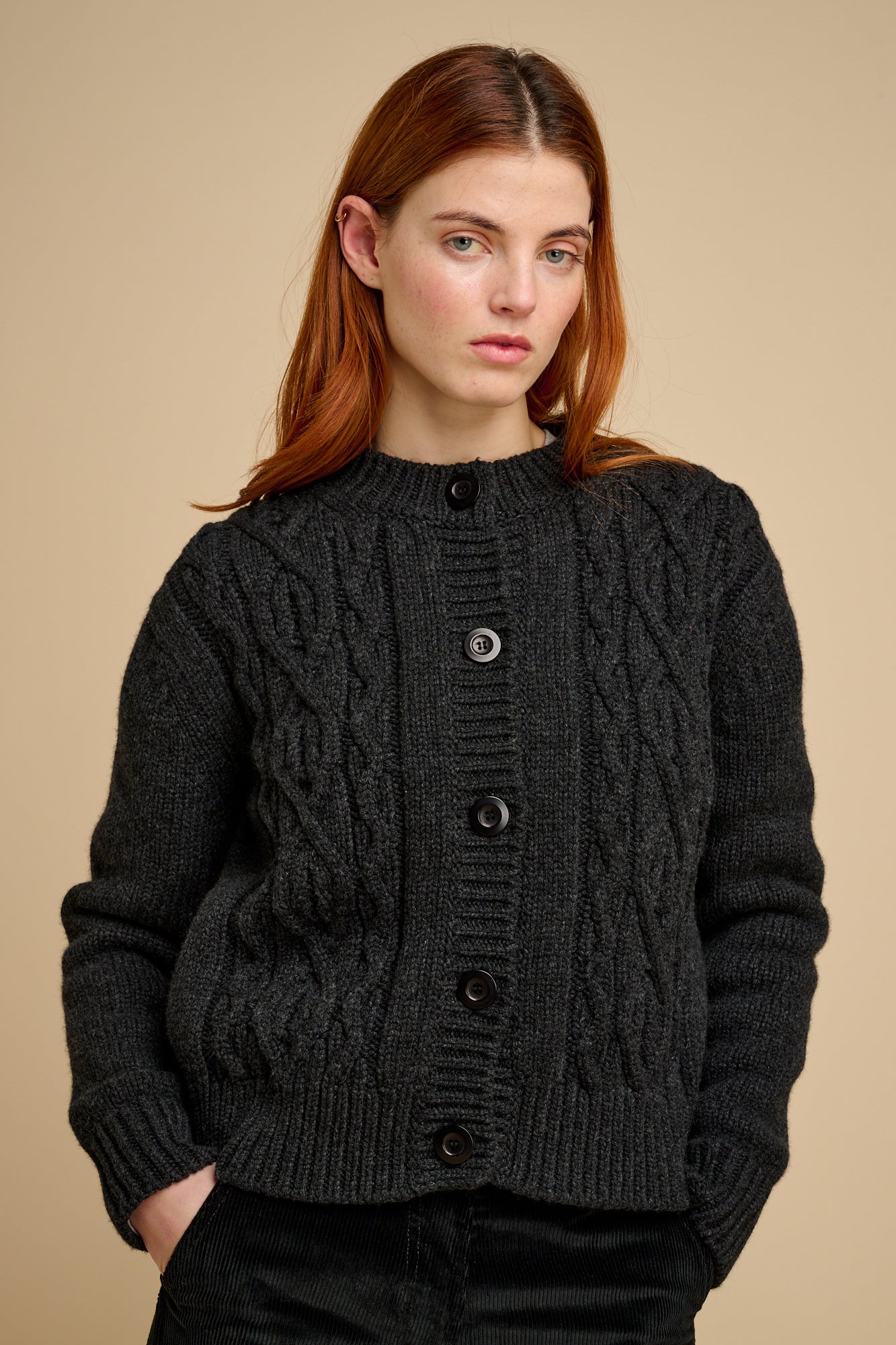 Woman wearing a dark grey knitted cardigan against a beige background