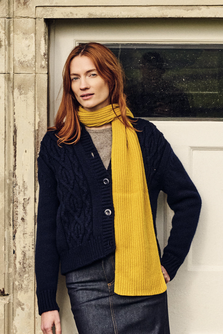 Woman wearing a navy cardigan and yellow scarf standing in front of a door.