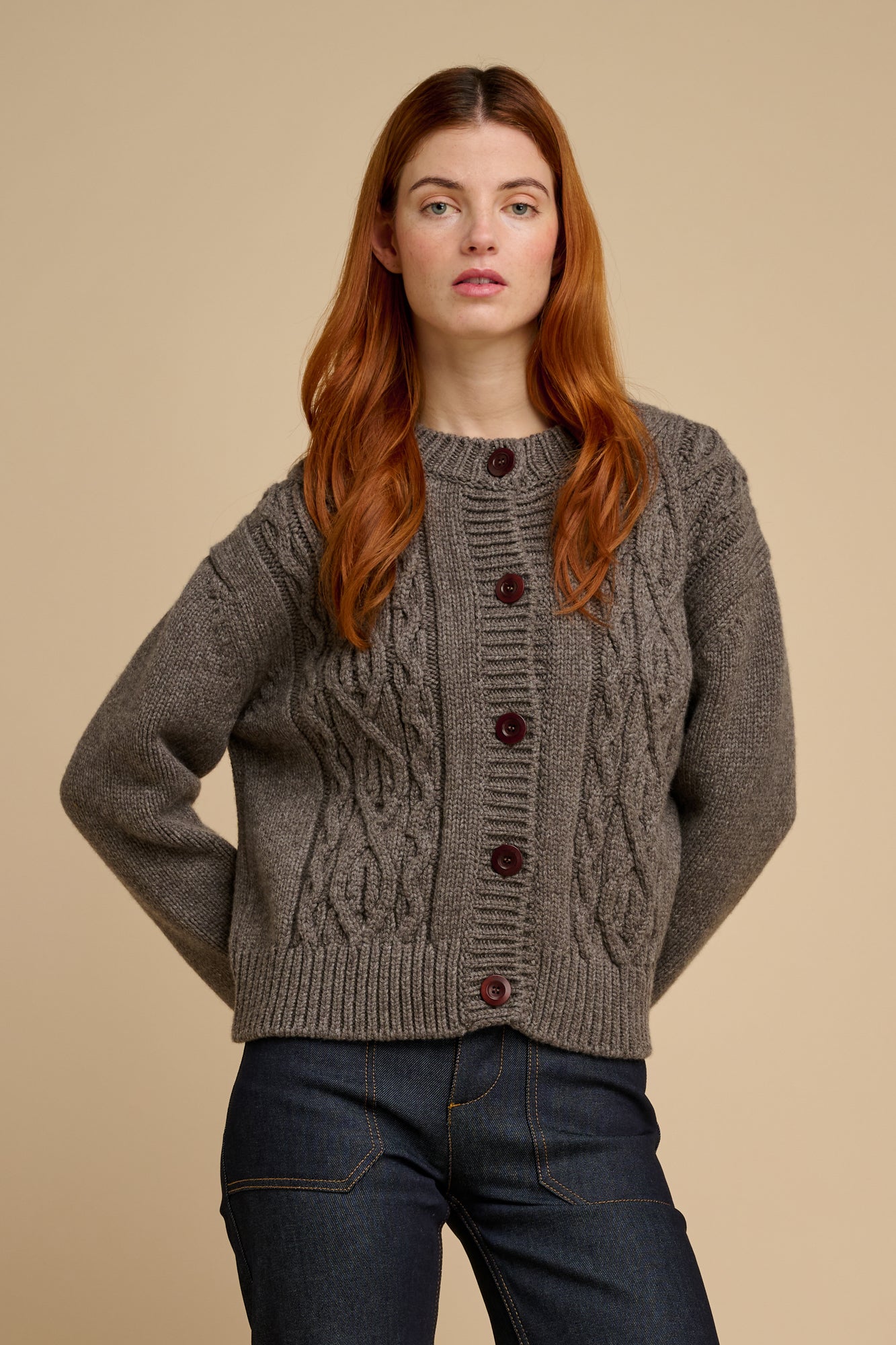 Woman wearing a truffle coloured cable knit cardigan with brown buttons on a beige background