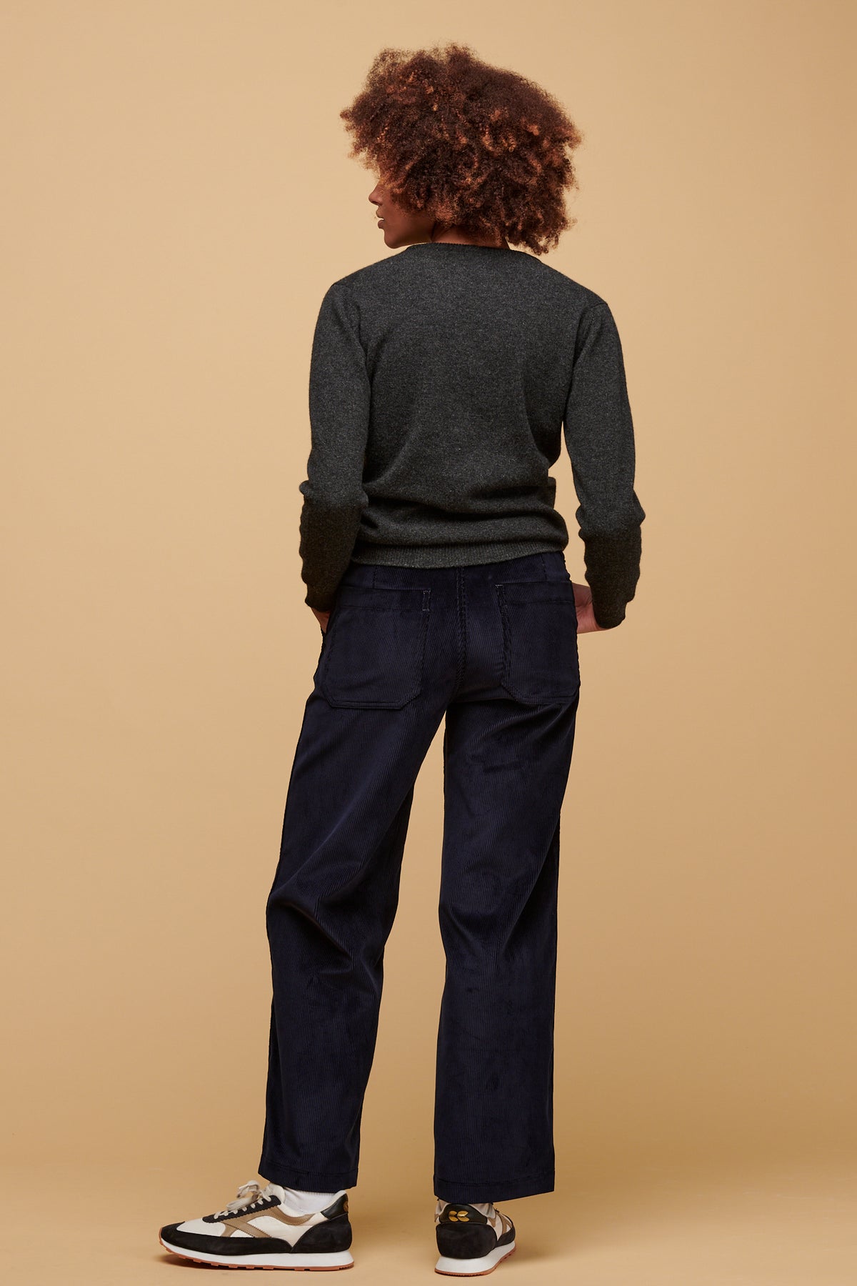 The back of female wearing women's corduroy work trousers in navy paired with lambswool crew neck in charcoal.