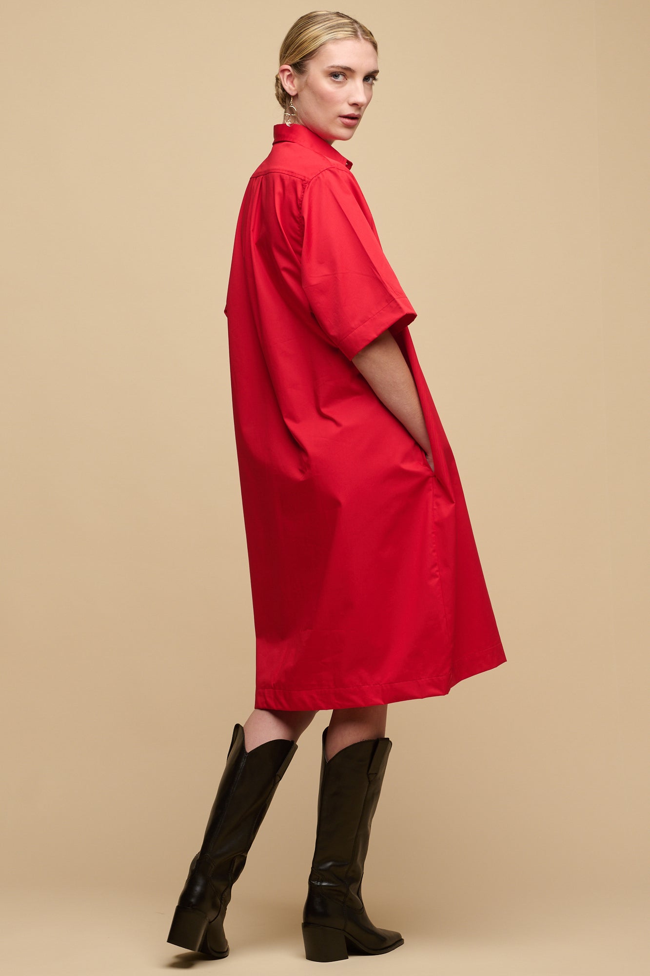 Back of female wearing unbelted cotton dress in red with hand in front pocket