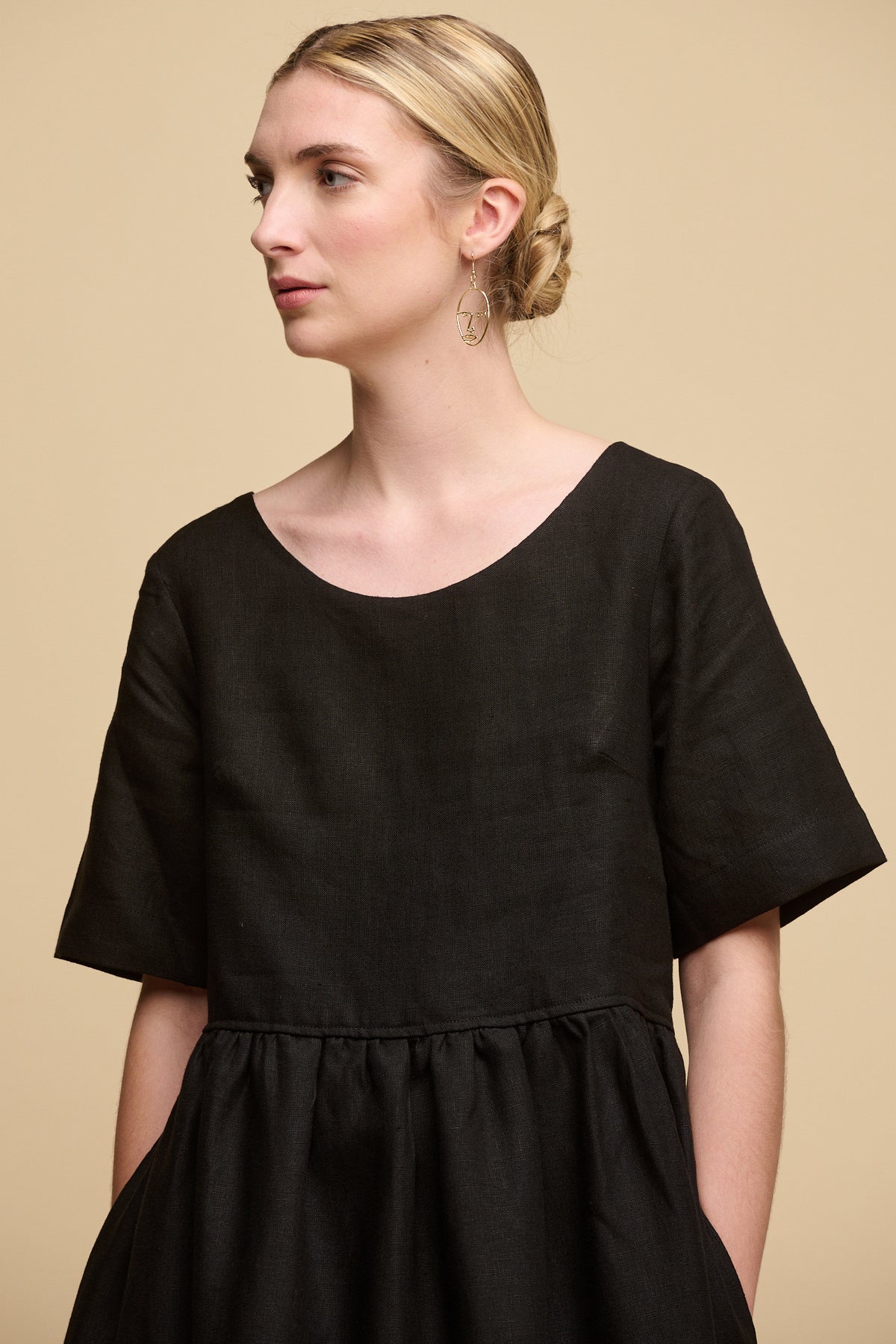 
            thigh up front image of female wearing crew neck gathered dress in black linen with hands in pockets