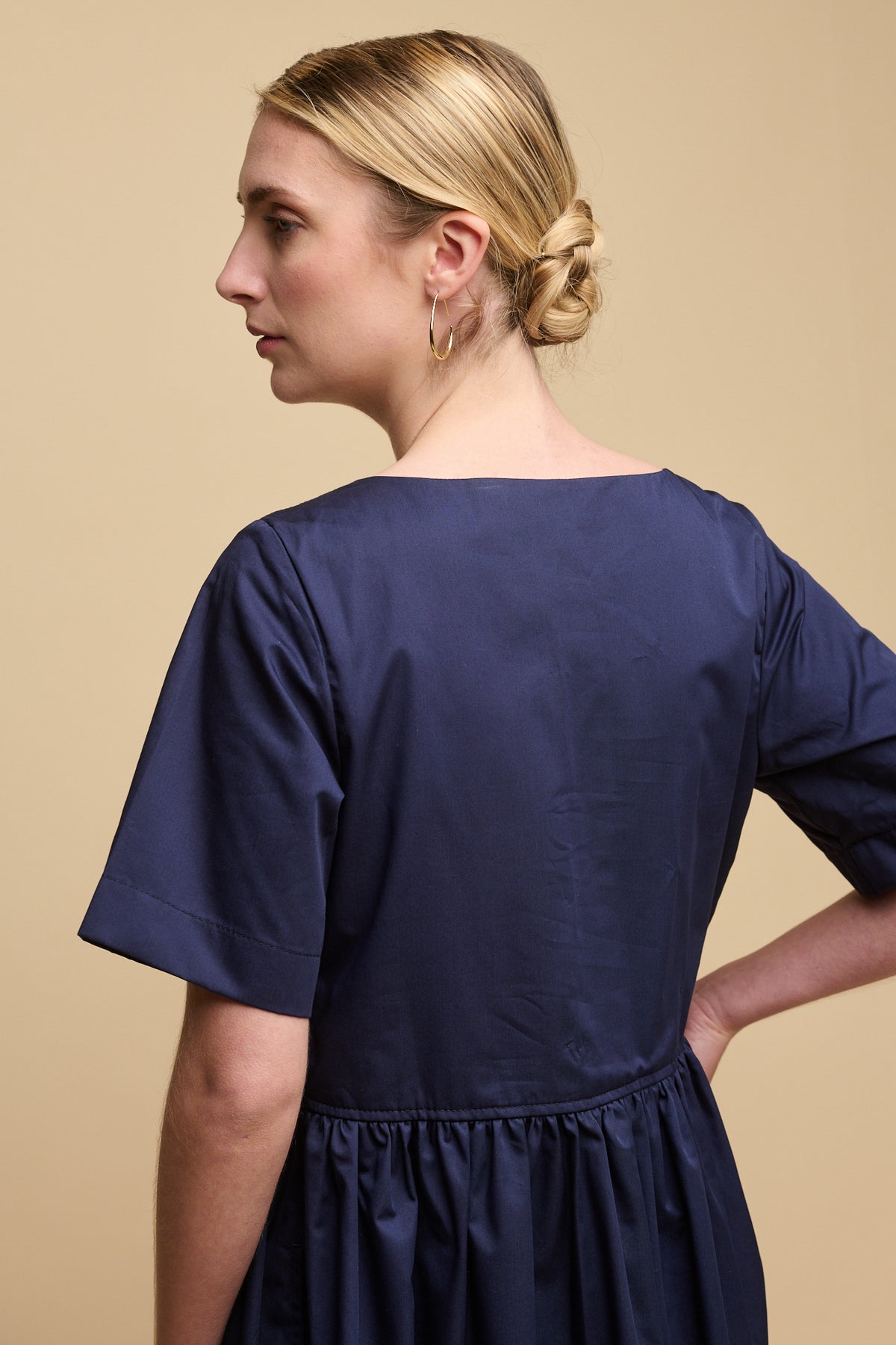 Hip up of the back of blonde female wearing crew neck gathered dress in navy