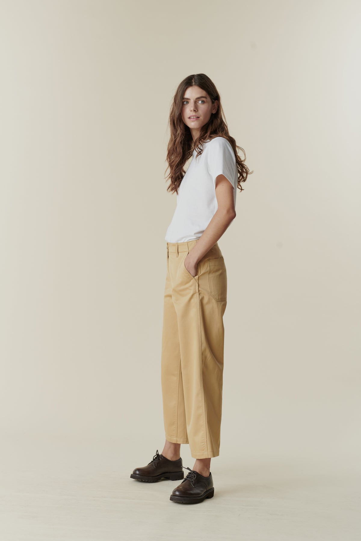 Front, full body image of brunette female wearing cropped work trousers in beige