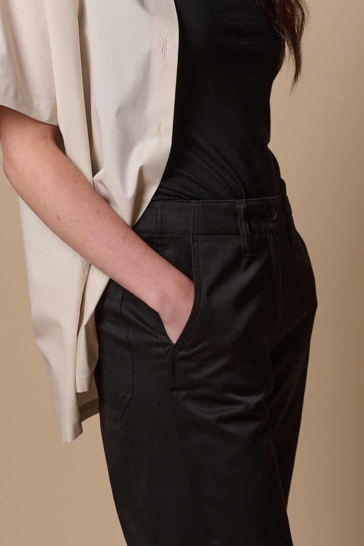 Close up of female wearing cropped work trousers in black with hand in front pocket, and waistband detail with belt loops