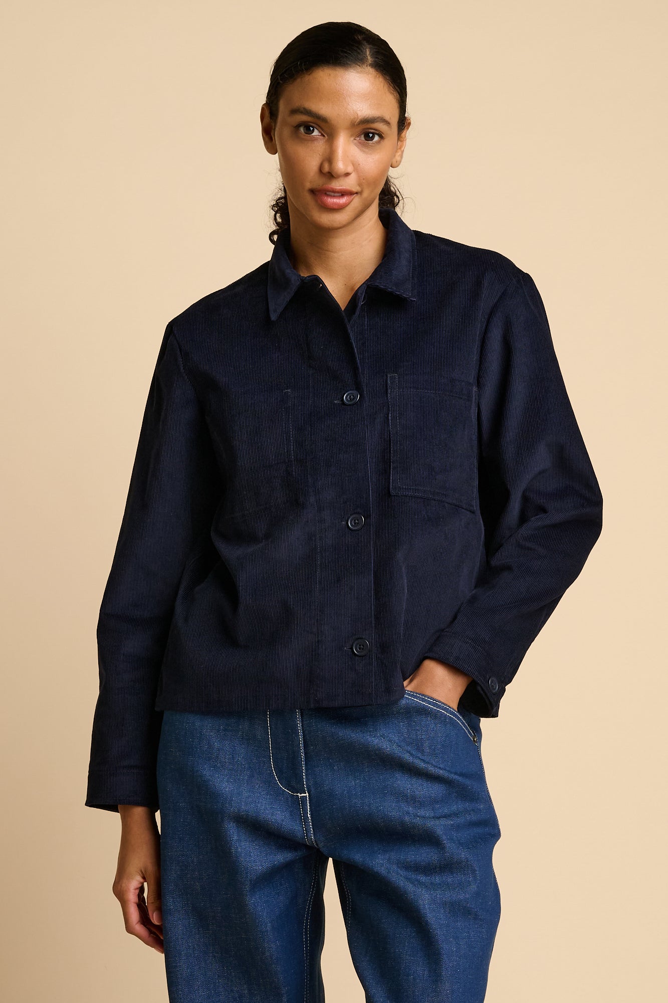 Woman wearing a navy overshirt and blue jeans on a beige background