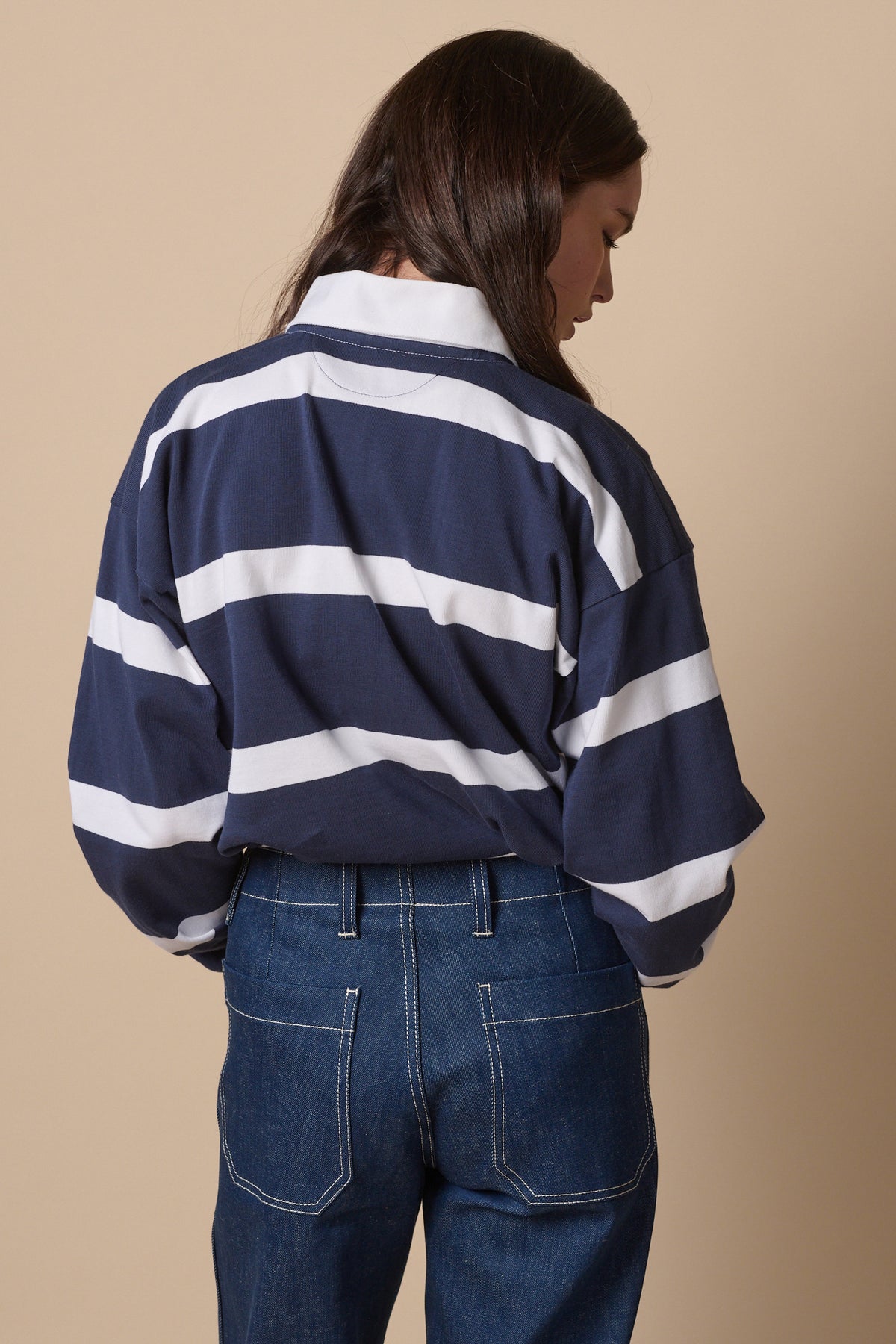 Back of female wearing fine stripe rugby shirt in navy white tucked into work jeans in blue