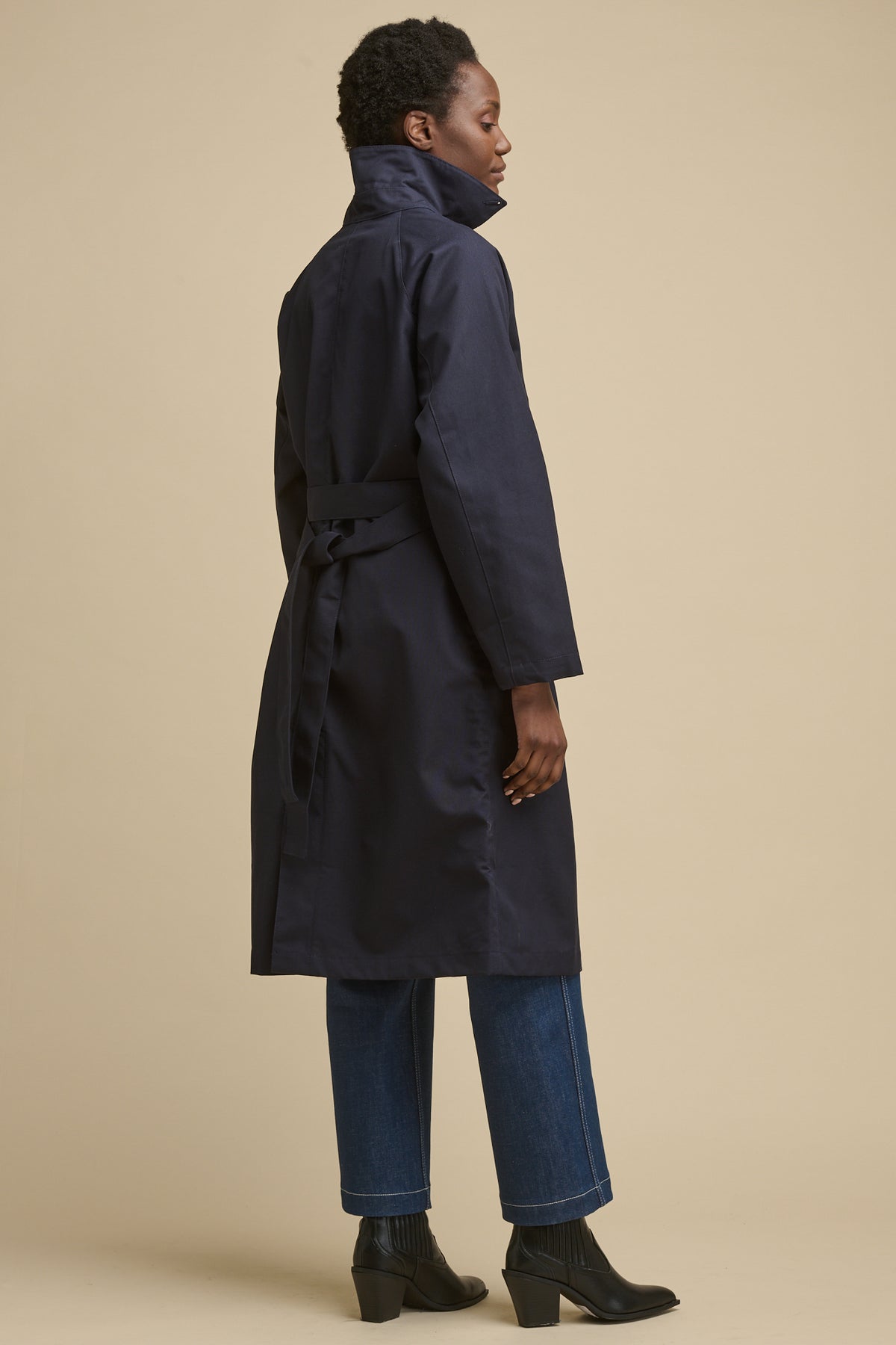 
            Full body image of the back of female wearing women&#39;s Frances Raglan Belted Raincoat in navy with belt tied at the back and collar up